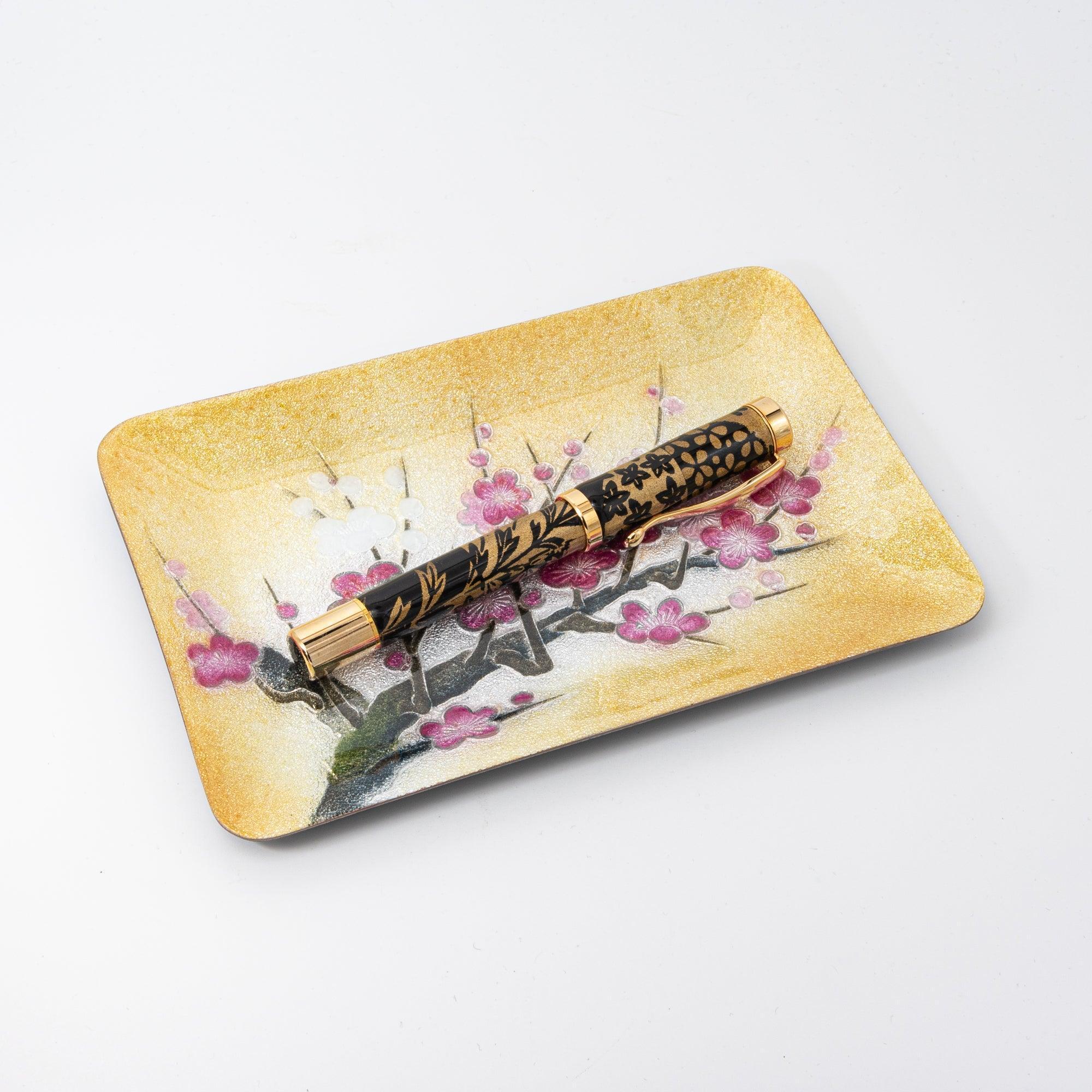 A close-up of a black and gold fountain pen on a plum blossom-themed tray with a golden backdrop, perfect for Japanese stationery enthusiasts.
