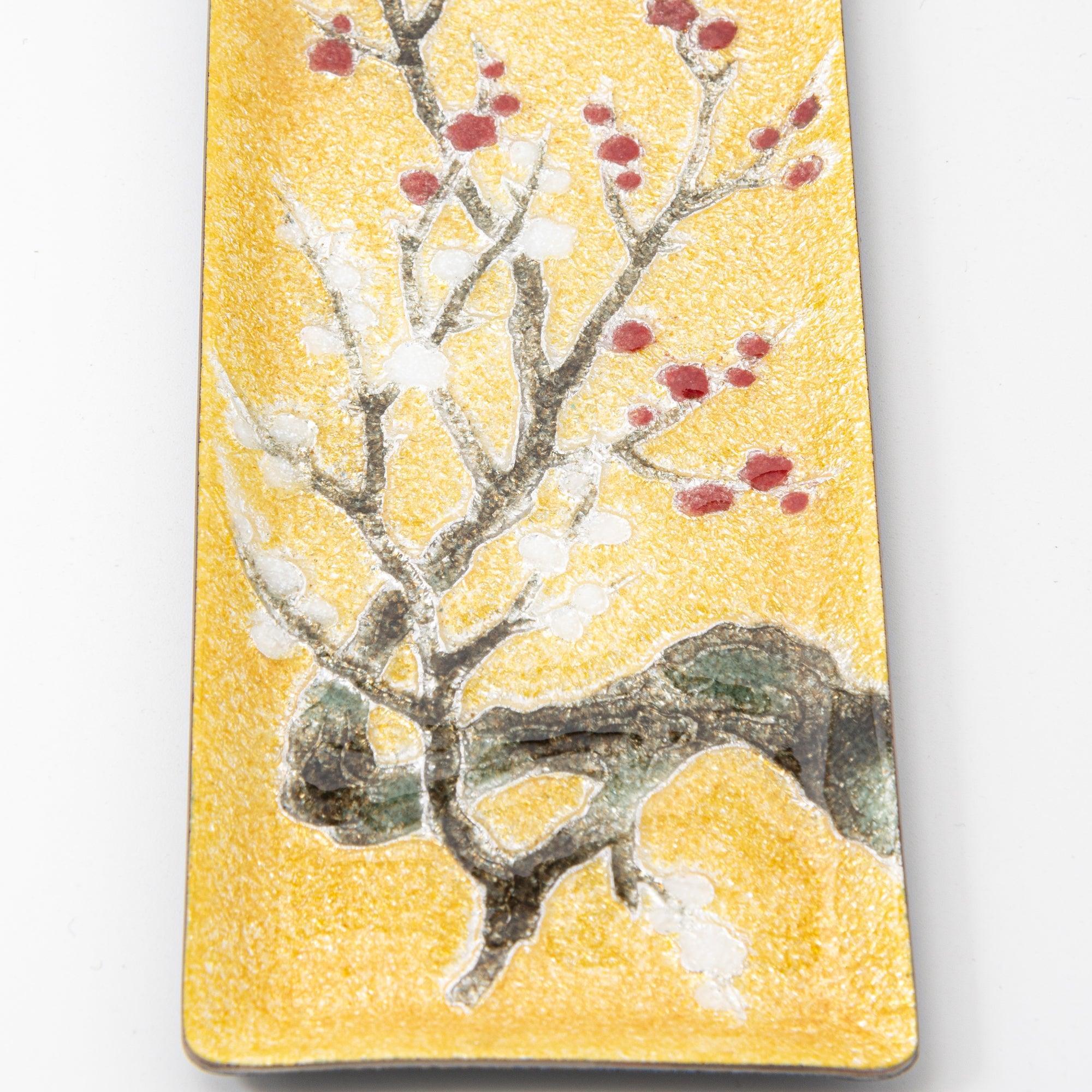 Close-up of lower section of gold enamel tray showing plum trunk, green rock, and white blossom clusters with red buds