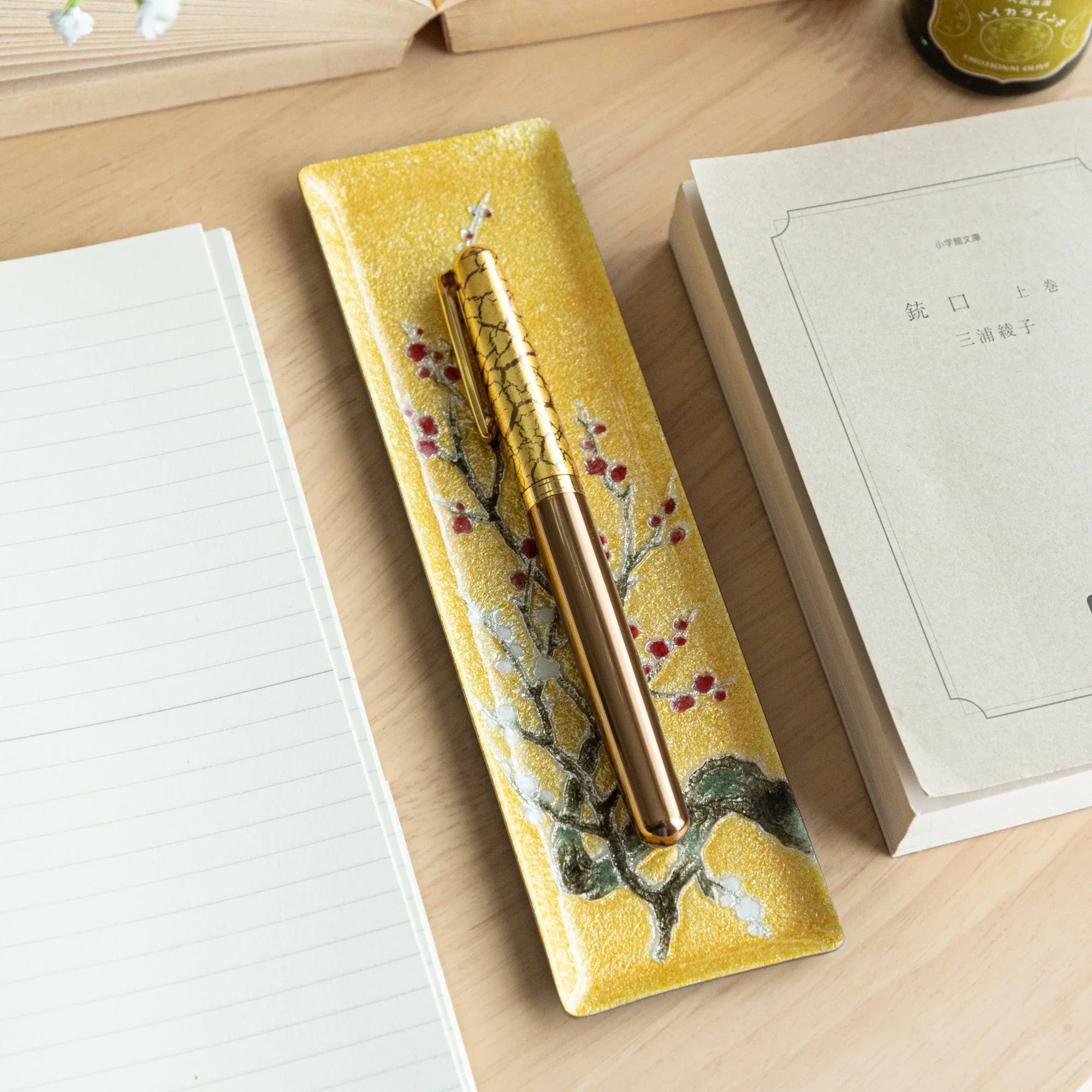 Gold enamel slim pen tray with plum branch and red berry design, gold crackle fountain pen on tray, wood desk with notebook