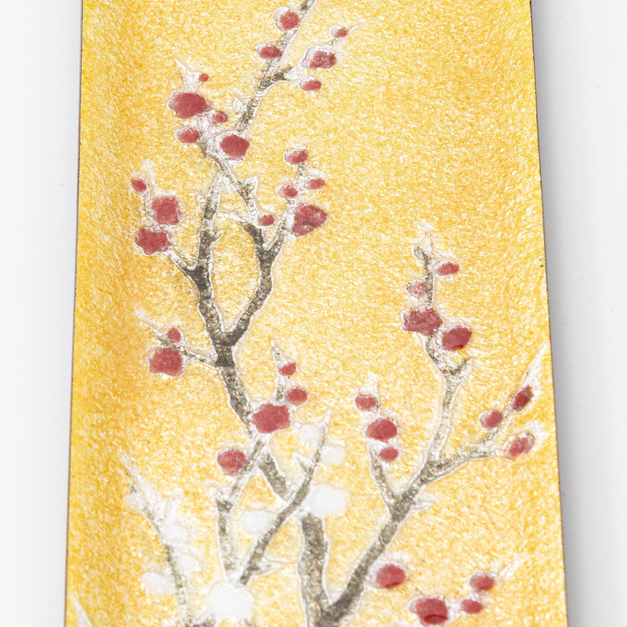 Close-up of gold enamel tray showing plum branches with red buds and white blossoms on gold shimmer background
