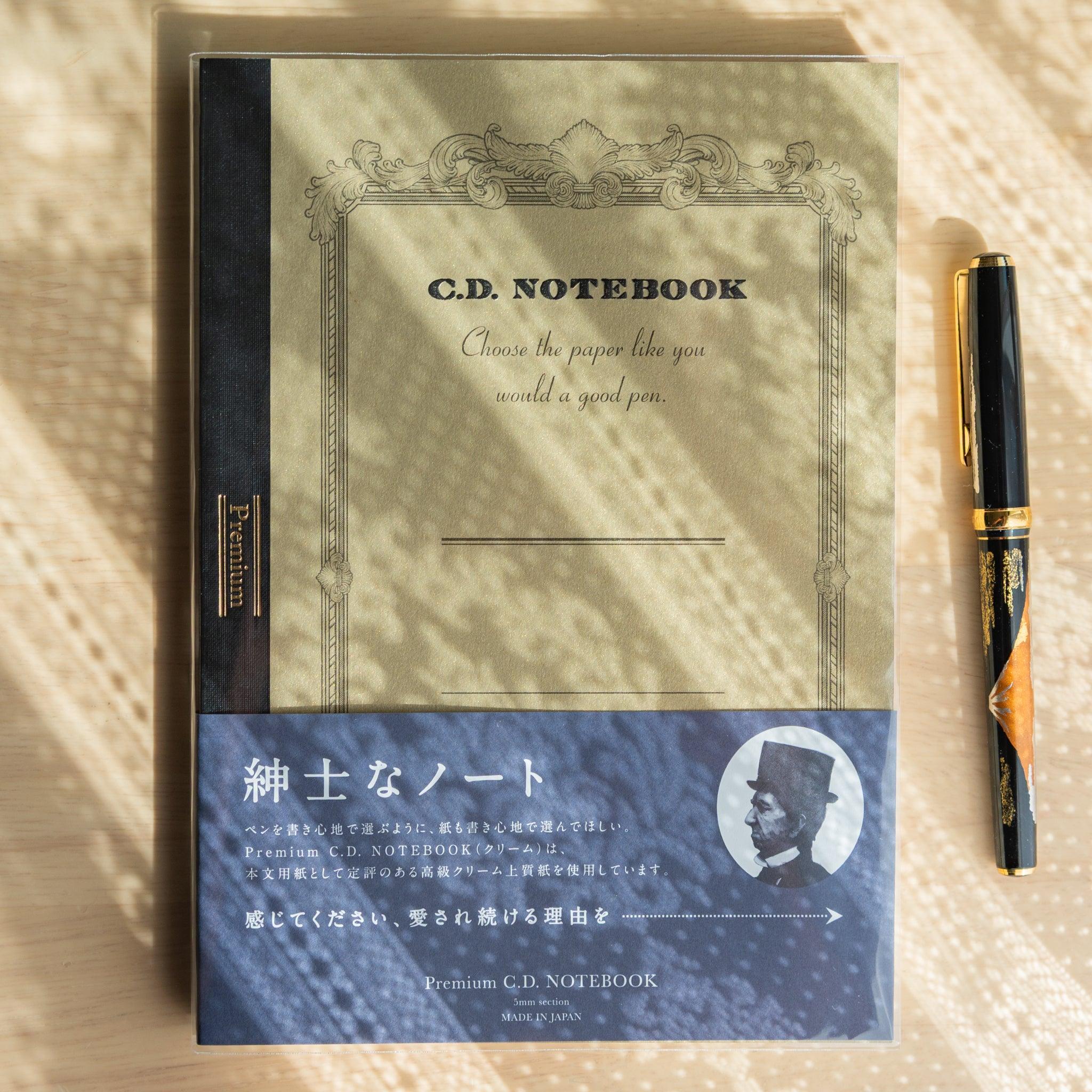 Front view of a gold Premium C.D. Japanese notebook with navy band and fountain pen, part of luxury Japanese stationery.