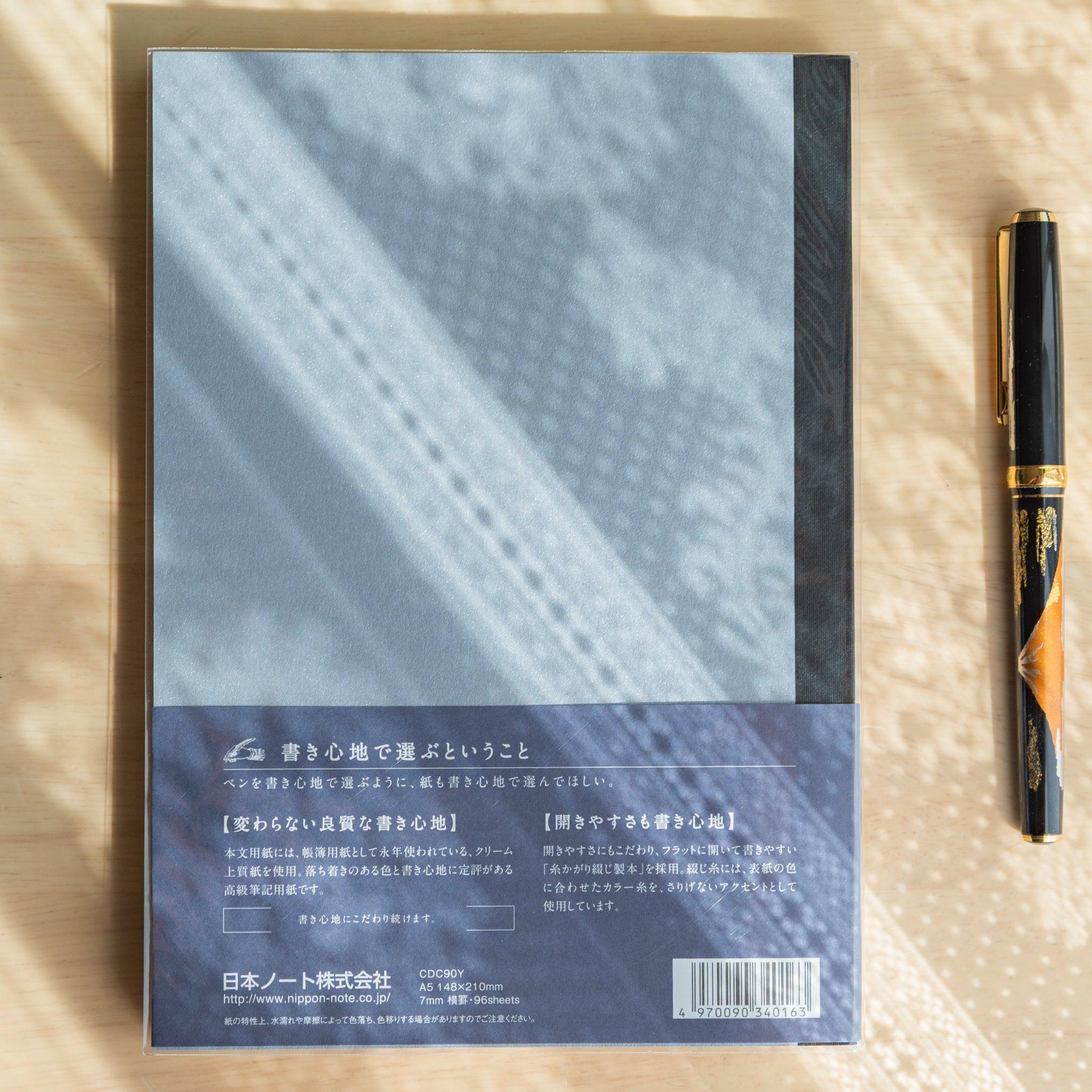 Back of blue Premium C.D. Japanese notebook with specs and fountain pen beside it, highlighting quality stationery details.
