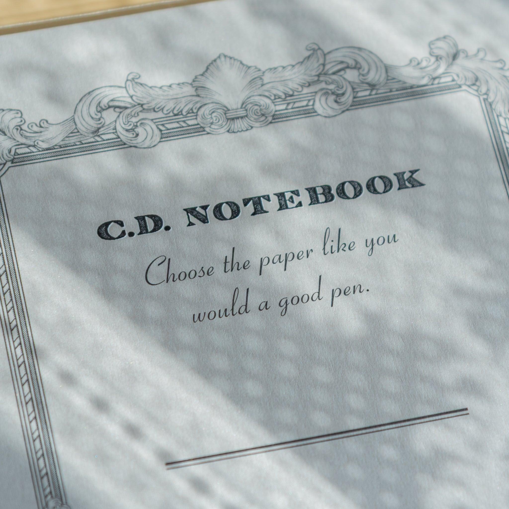 Close-up of a Japanese notebook cover showing the quote “Choose the paper like you would a good pen,” from the Premium C.D. NOTEBOOK series