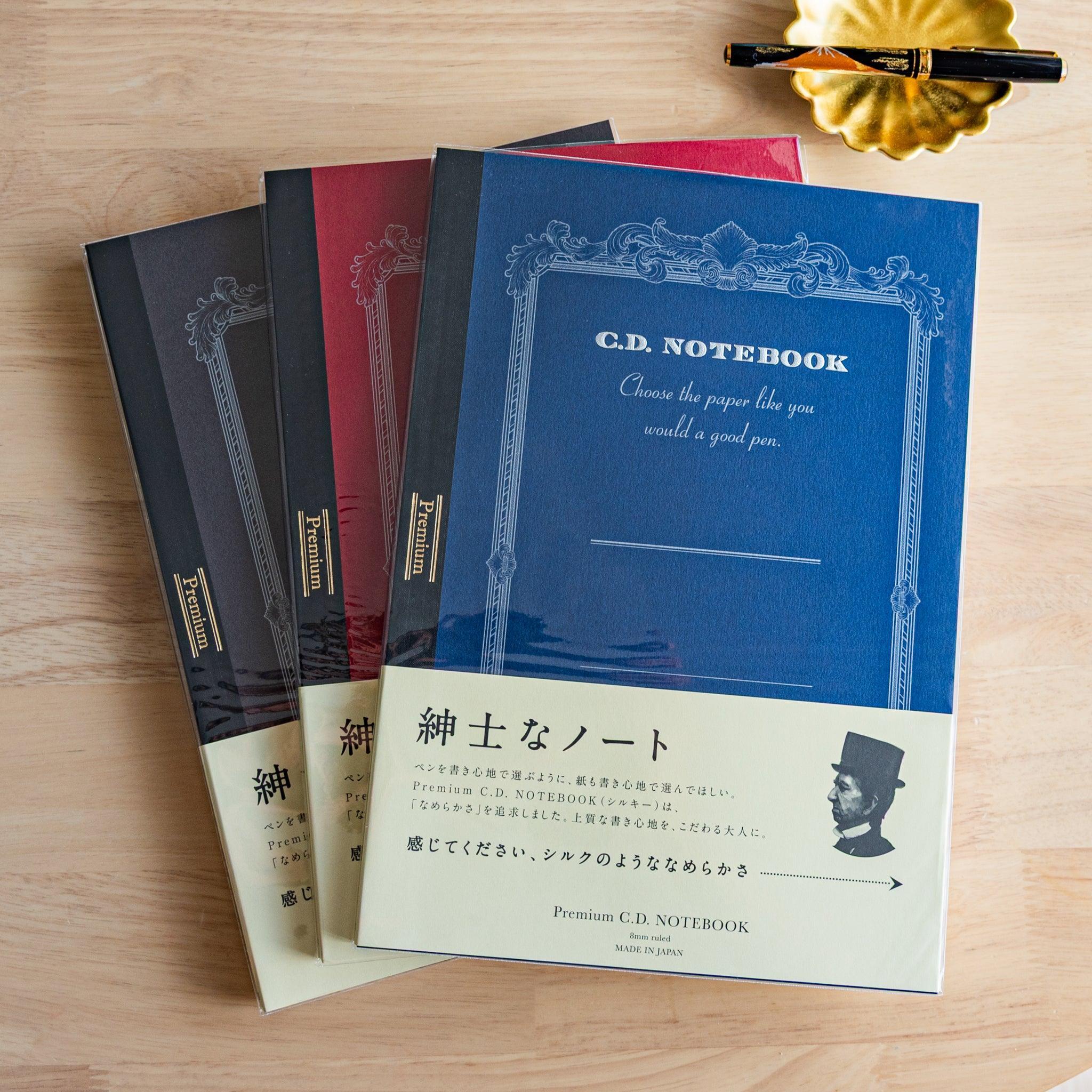 Three Premium CD Japanese notebooks in black, red, and blue covers with a fountain pen, showcasing refined Japanese stationery