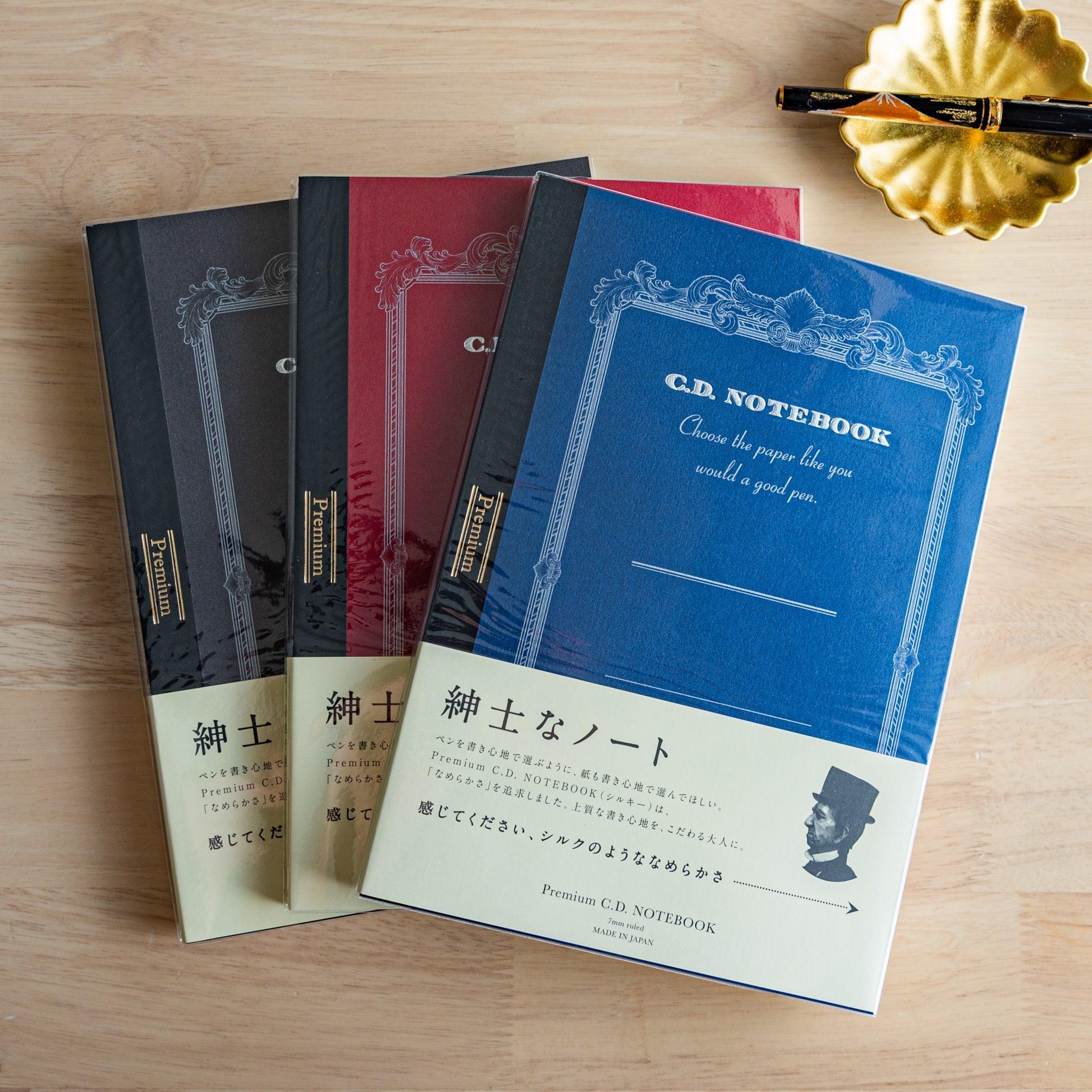 Three Premium CD Japanese notebooks in black, red, and blue covers with a fountain pen, showcasing refined Japanese stationery
