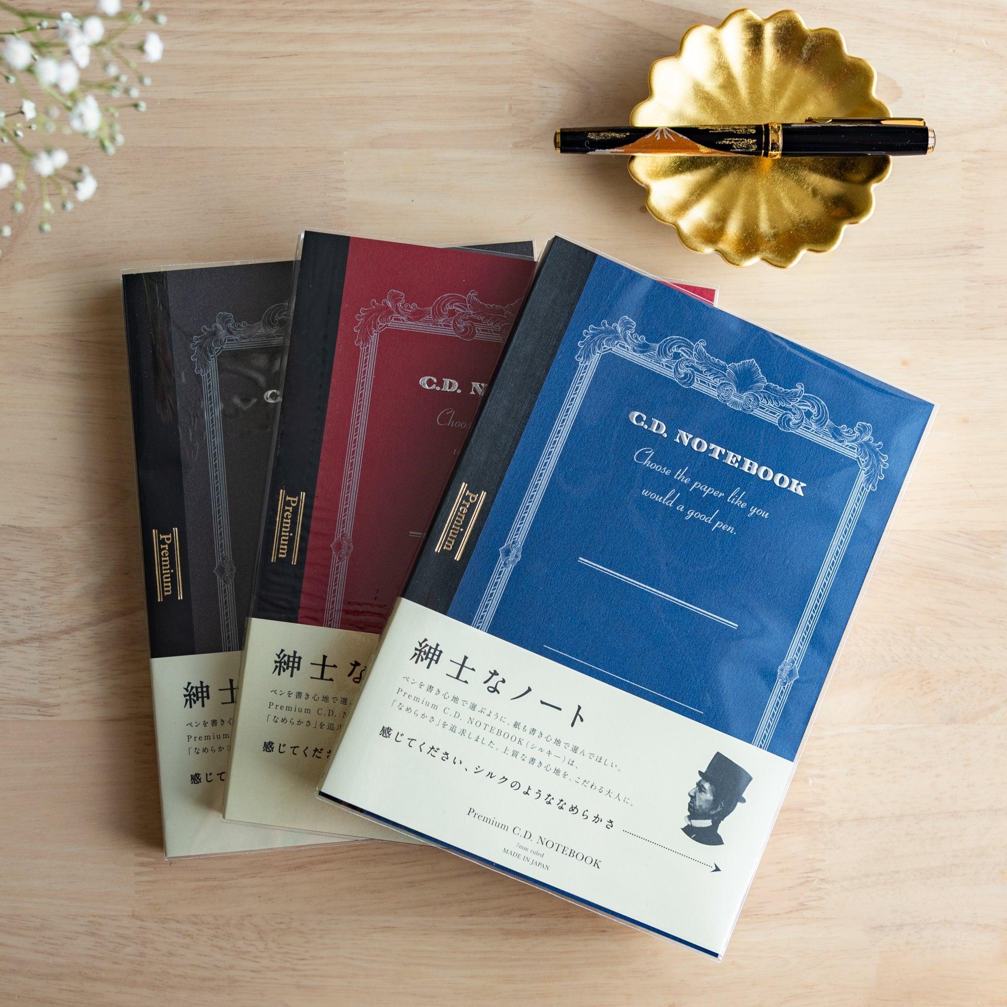 Three Premium CD Japanese notebooks in black, red, and blue covers with a fountain pen, showcasing refined Japanese stationery