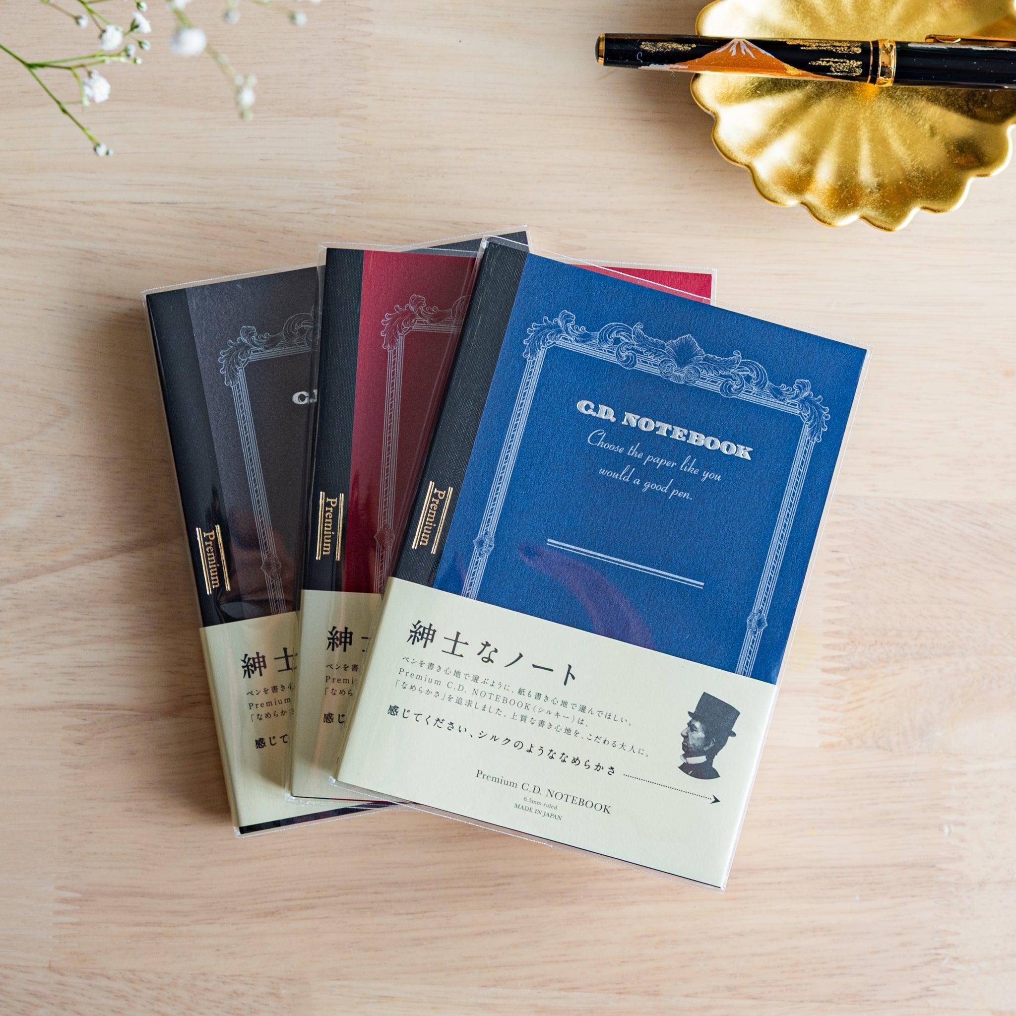 Three Premium CD Japanese notebooks in black, red, and blue covers with a fountain pen, showcasing refined Japanese stationery