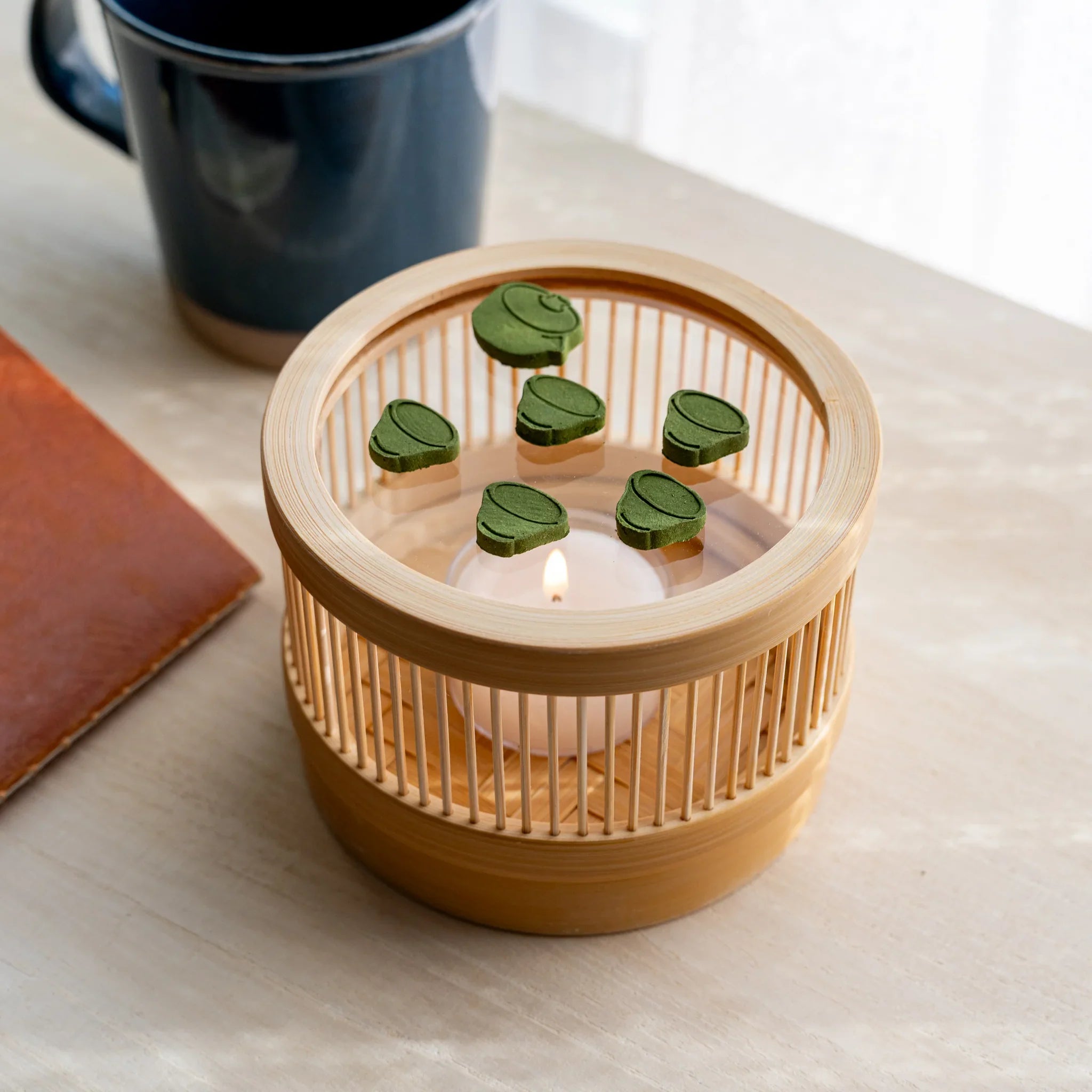 Top-down view of bamboo matcha incense tea warmer with teapot and tea cup pressed matcha pieces around a lit tealight