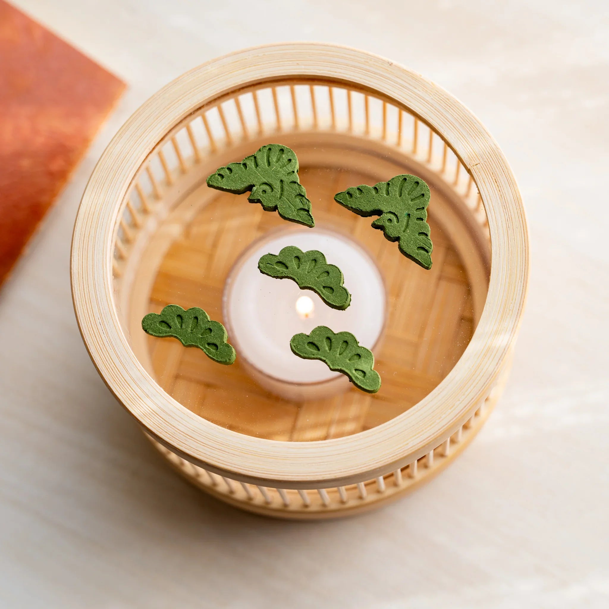Top-down view of bamboo matcha incense tea warmer with pine-sprig pressed matcha pieces around a lit tealight