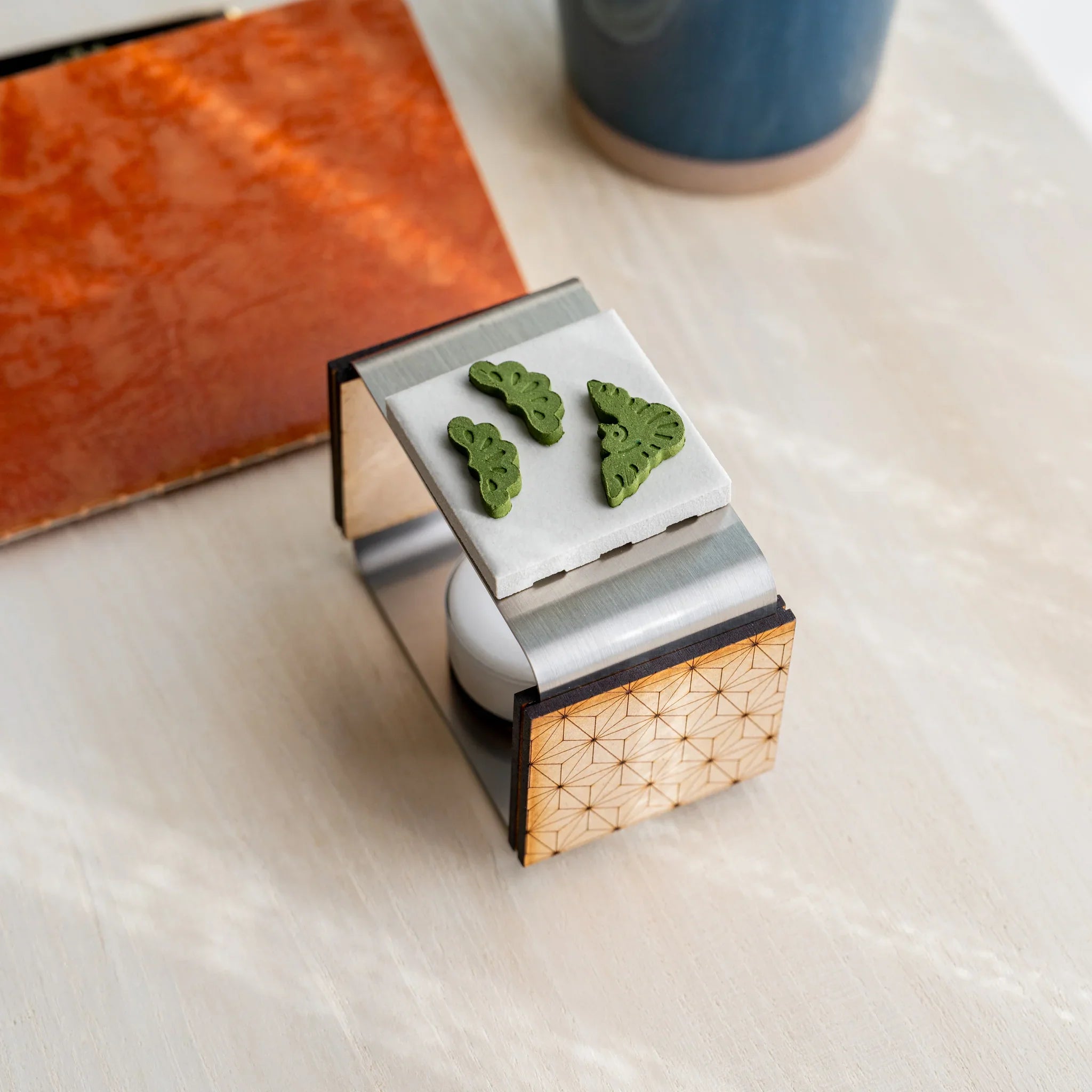 Foldable matcha incense tea warmer with asanoha wood and pine-sprig pressed matcha pieces on the ceramic plate