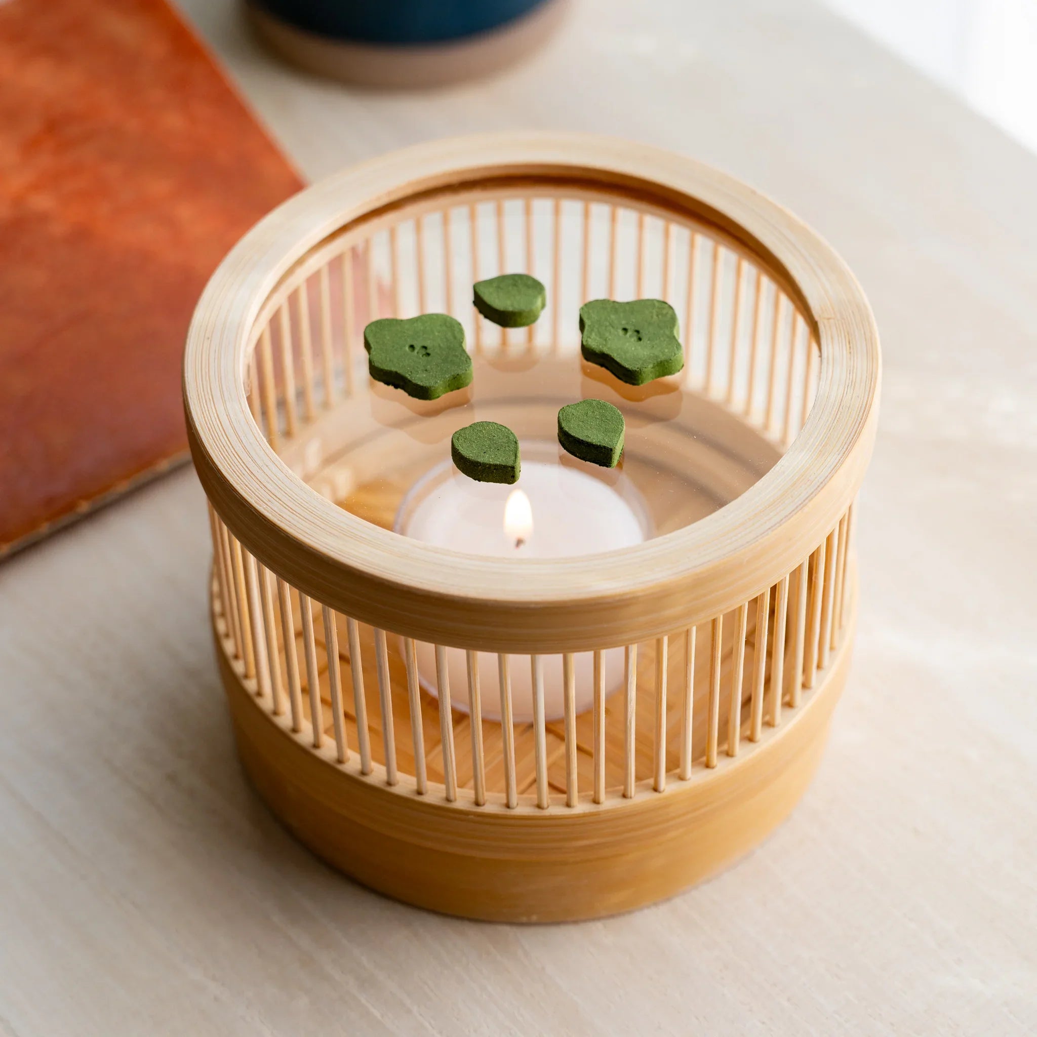 Top-down view of bamboo matcha incense tea warmer with plum-shape pressed matcha pieces around a lit tealight