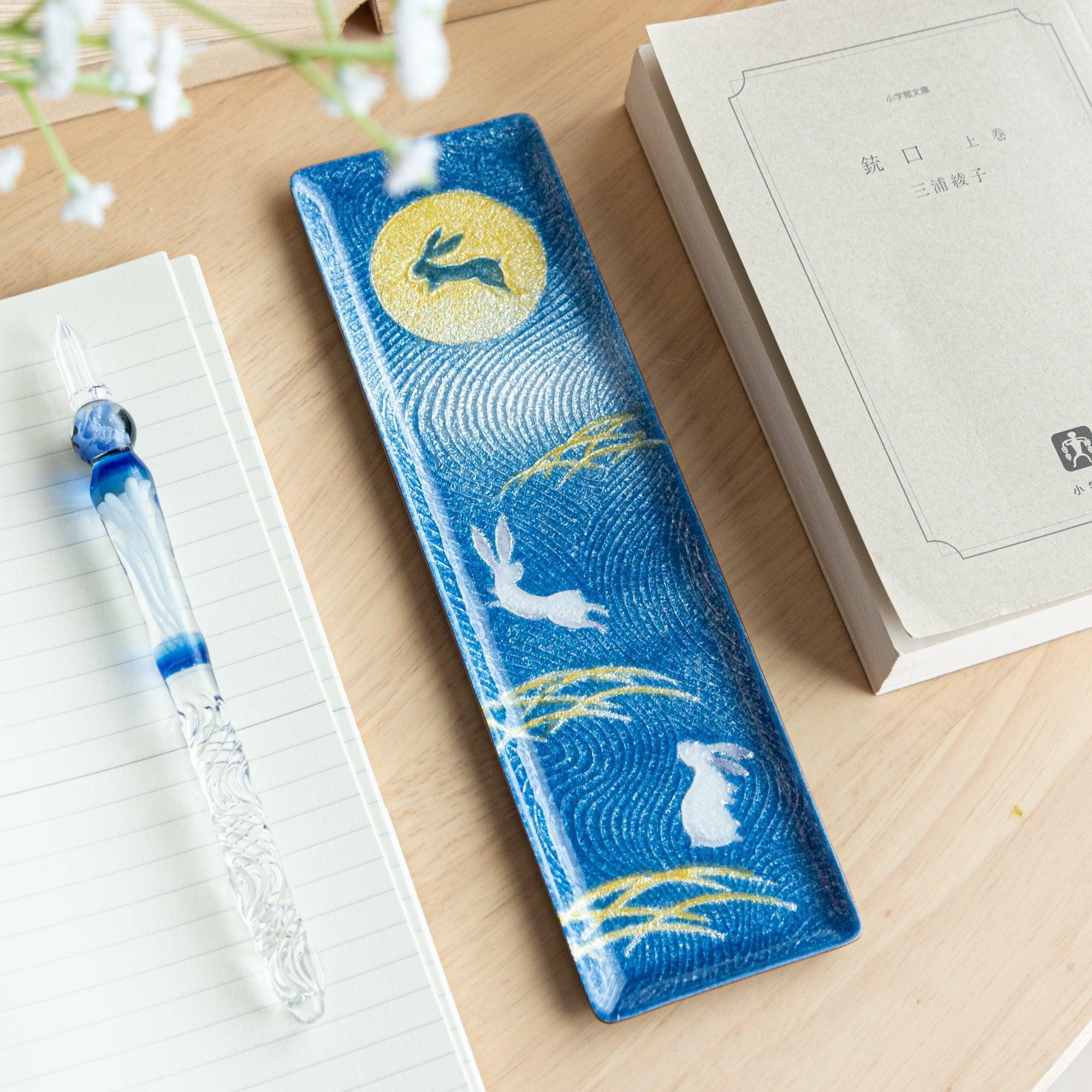 A blue Japanese stationery tray featuring a moonlit rabbit design, complemented by golden grass motifs and wavy textures.