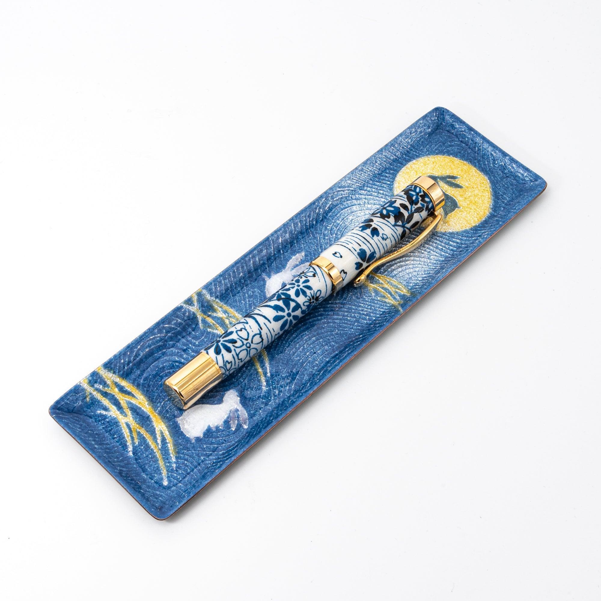 A blue Japanese stationery tray with a moonlit rabbit motif and golden grass, paired with a floral-designed fountain pen.