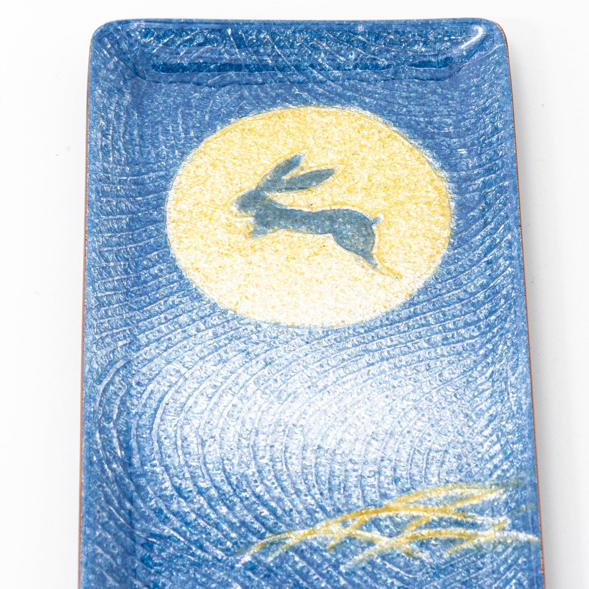 A close-up of a blue Japanese stationery tray showcasing a rabbit silhouette against a golden full moon.