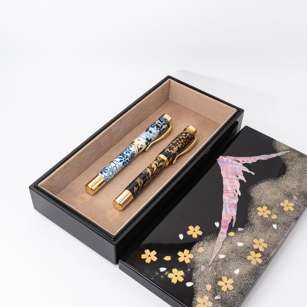 Open lacquer pen case with floral and Mt. Fuji design, holding two gold-accented pens with intricate patterns, showcasing Japanese stationery craftsmanship.