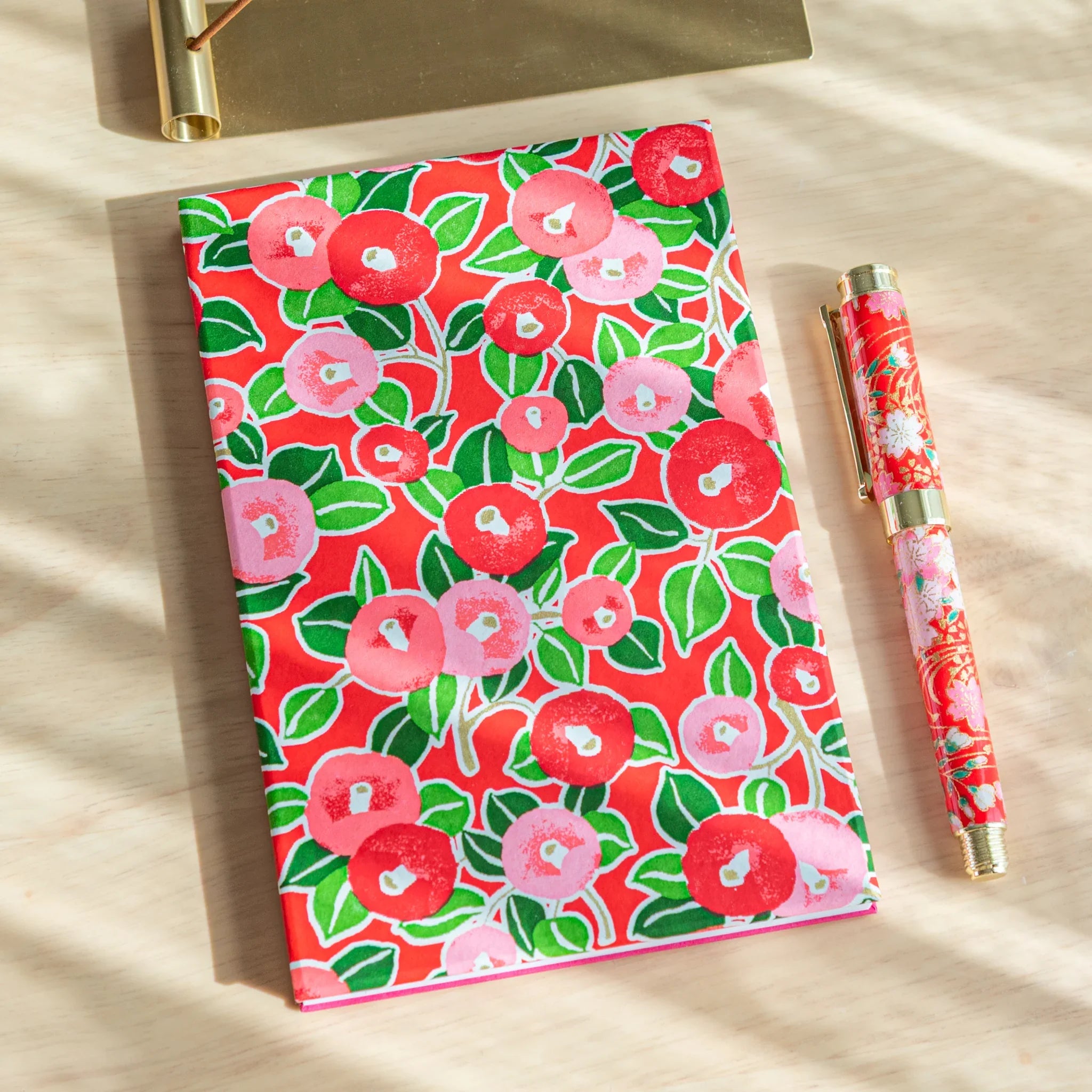 Red Camellia washi goshuincho front cover showing red and pink camellia blooms with green leaves, displayed with matching pen