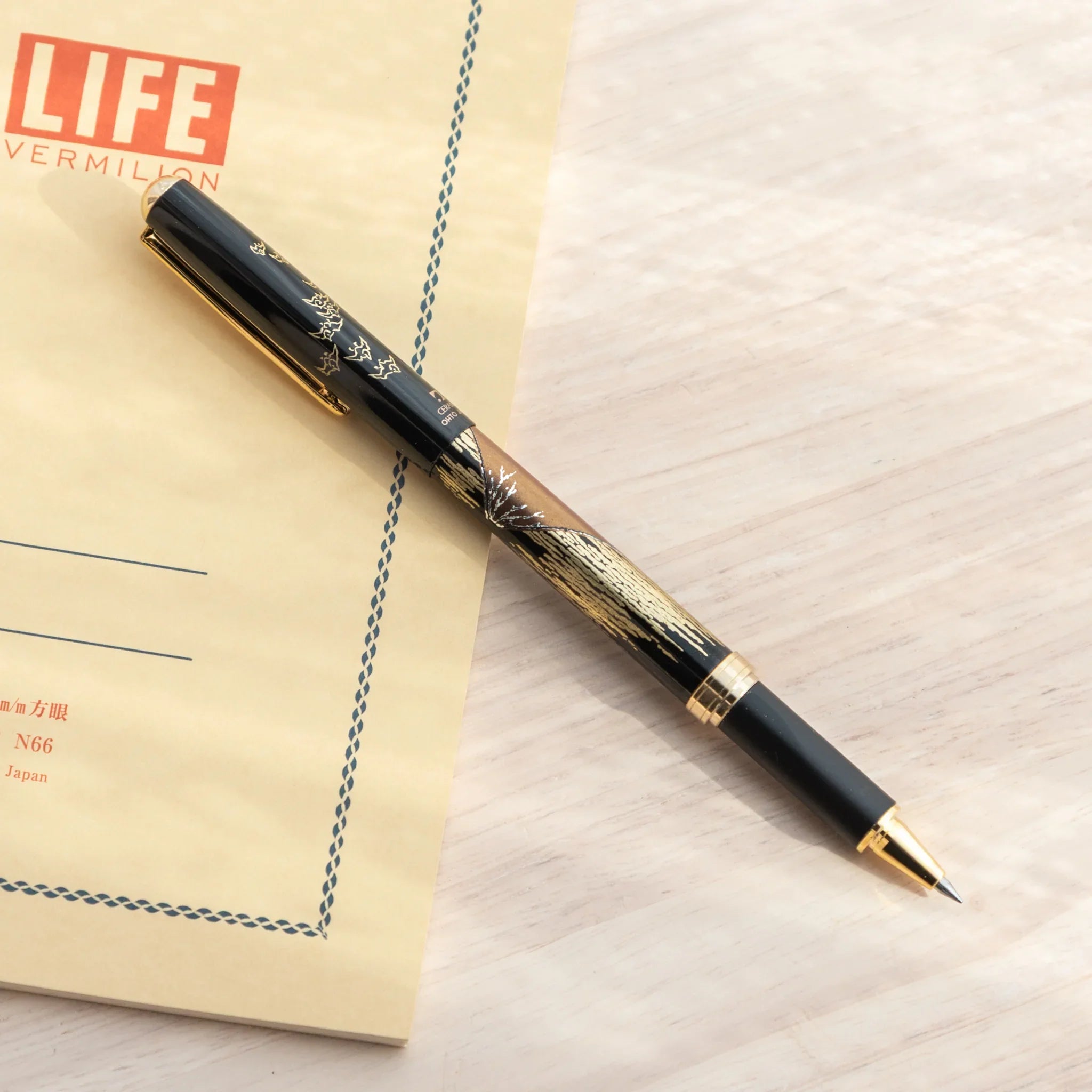 Uncapped Japanese Ballpoint Pen with Lacquer Red Fuji design placed on a desk with a notebook.