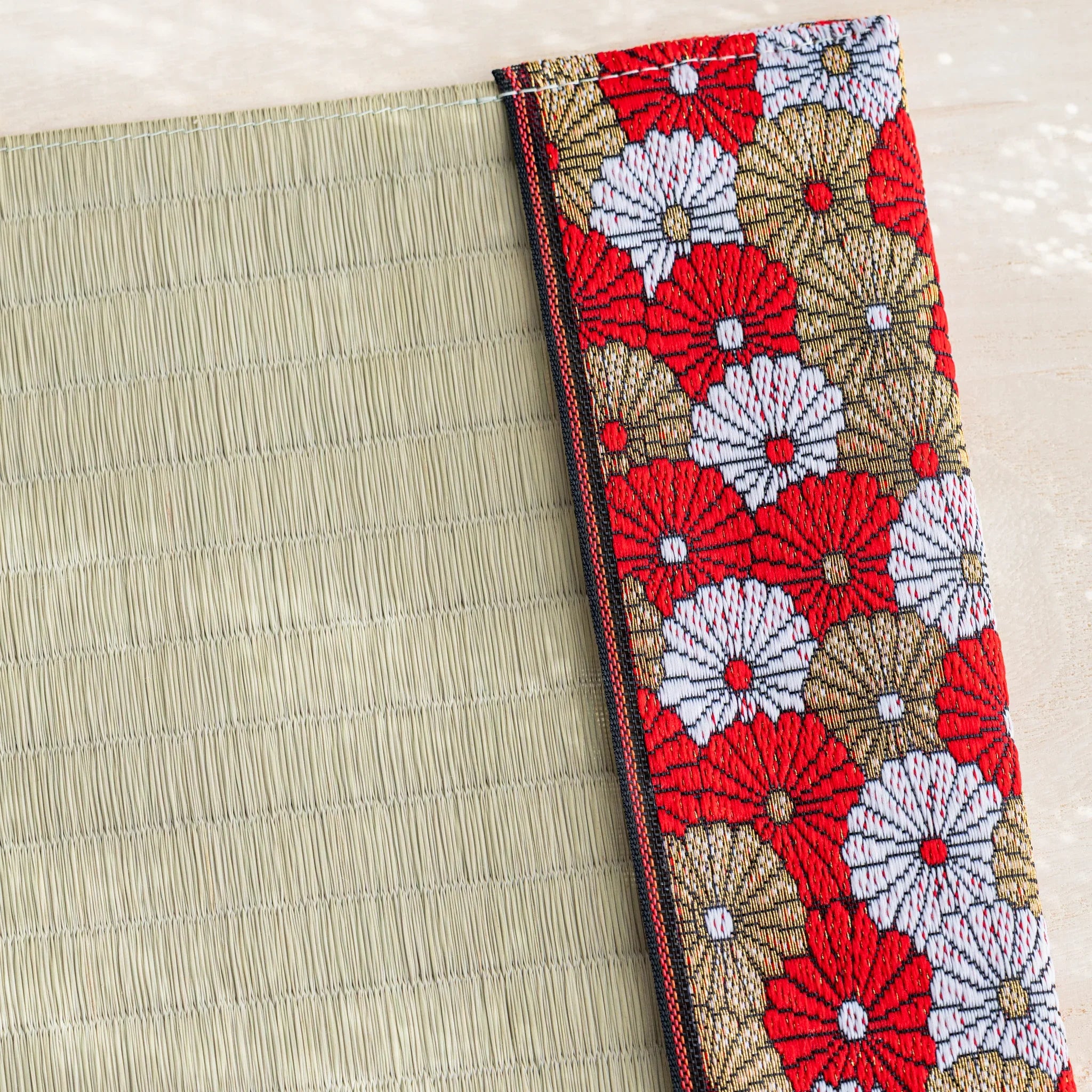 Close-up of chrysanthemum brocade band with black and red striped trim next to woven green rush straw