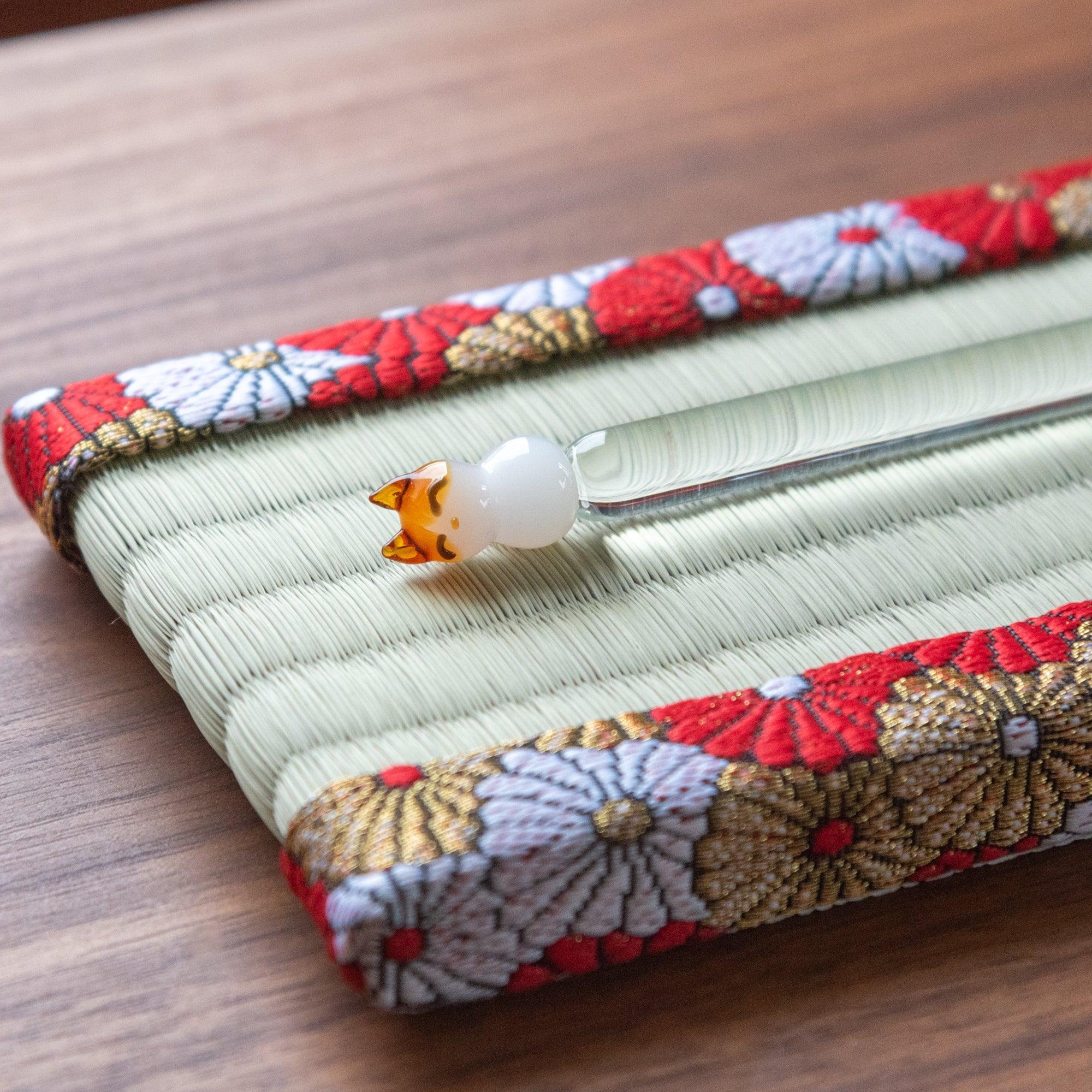 Japanese tatami pen tray with chrysanthemum brocade border holding a glass dip pen with cat figurine, close-up angled view