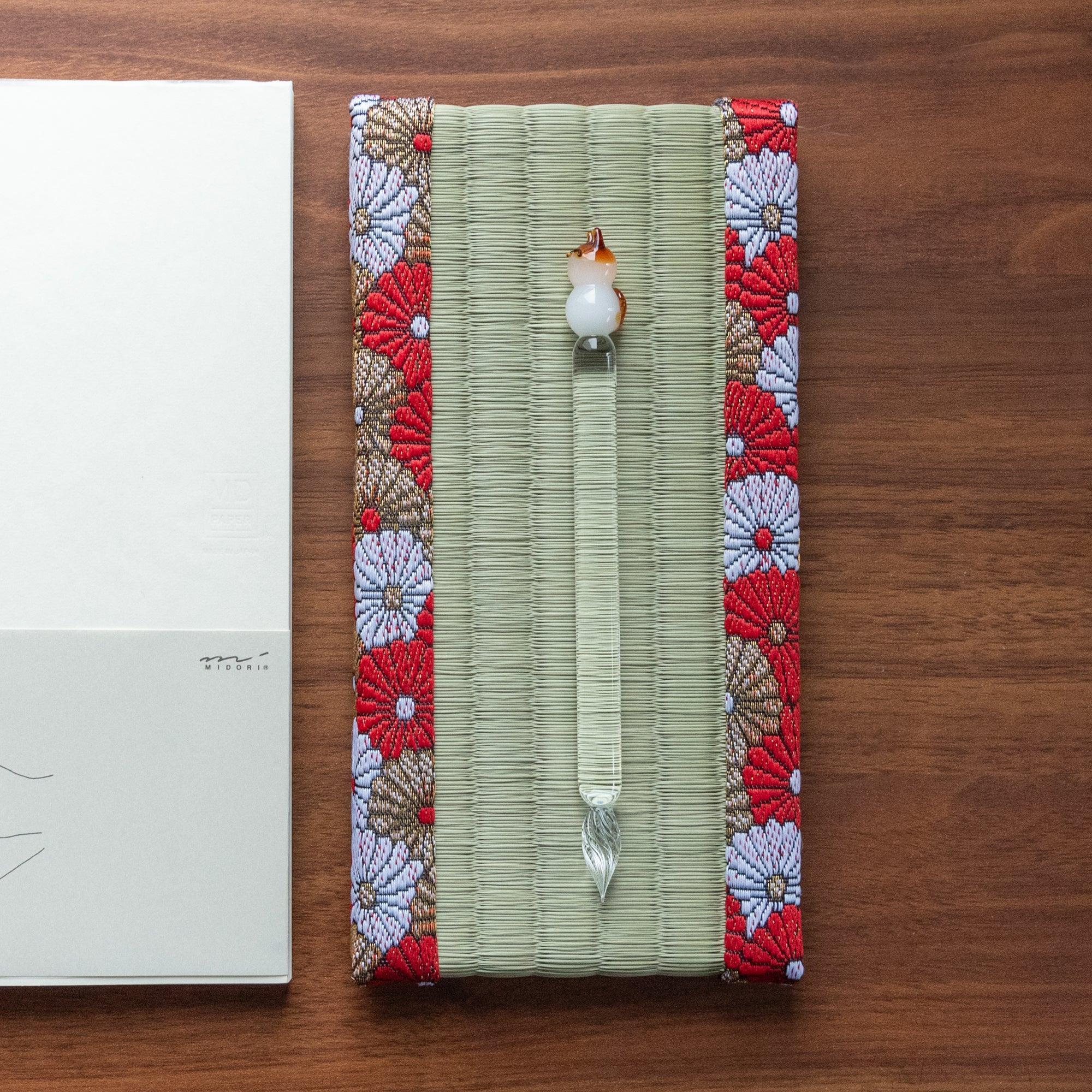 Japanese tatami pen tray with chrysanthemum brocade border holding a cat figurine glass dip pen, overhead view