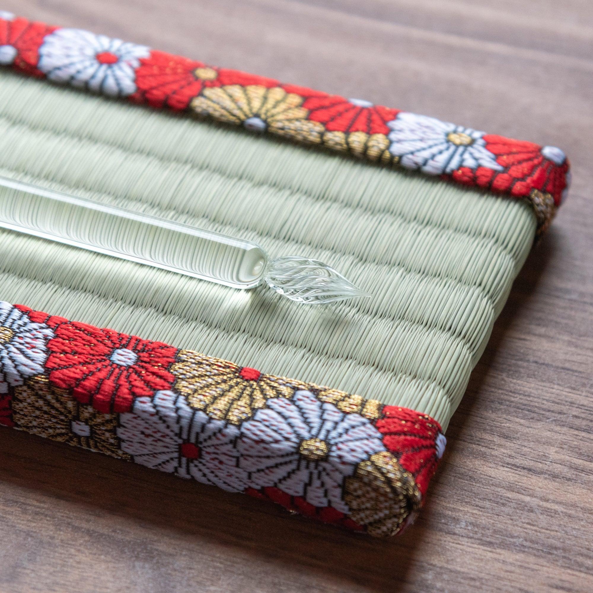 Close-up of Japanese tatami pen tray end showing glass dip pen nib on igusa rush weave surface and brocade border