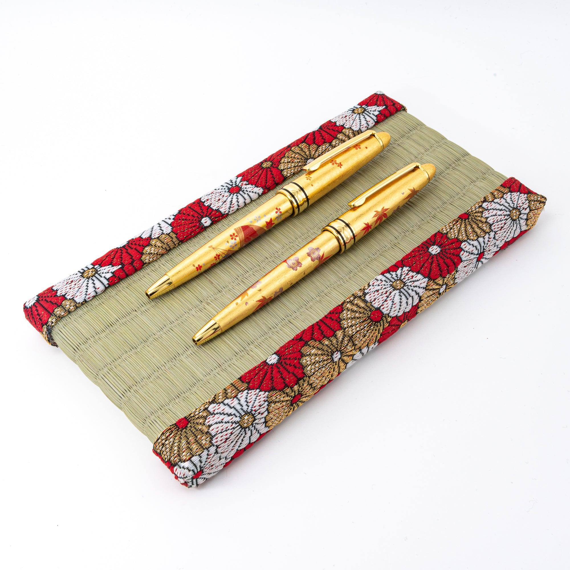 Japanese tatami pen tray with chrysanthemum brocade border holding two gold makie-style pens on white background
