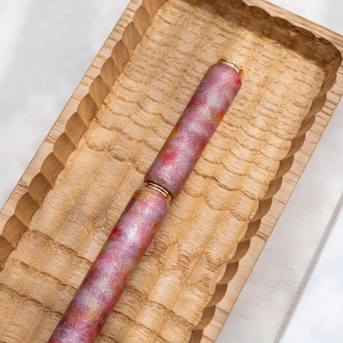 Red marbled urushi lacquered rollerball pen in zelkova wood, angled view in a carved wooden tray