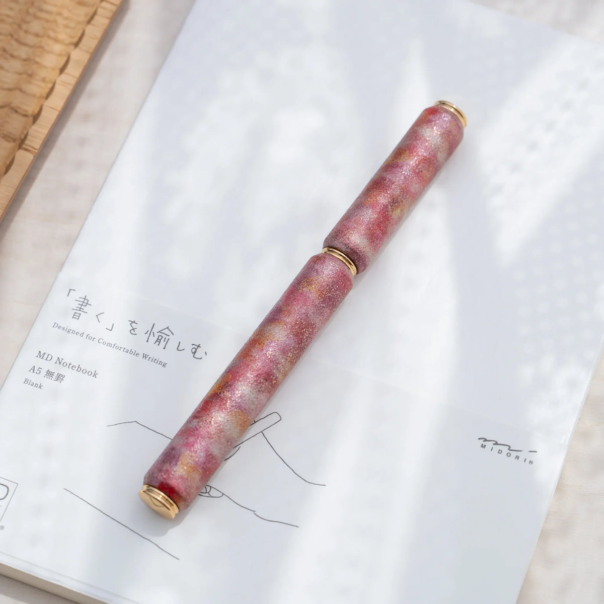 Red marbled urushi lacquered rollerball pen in zelkova wood, resting on a Japanese notebook