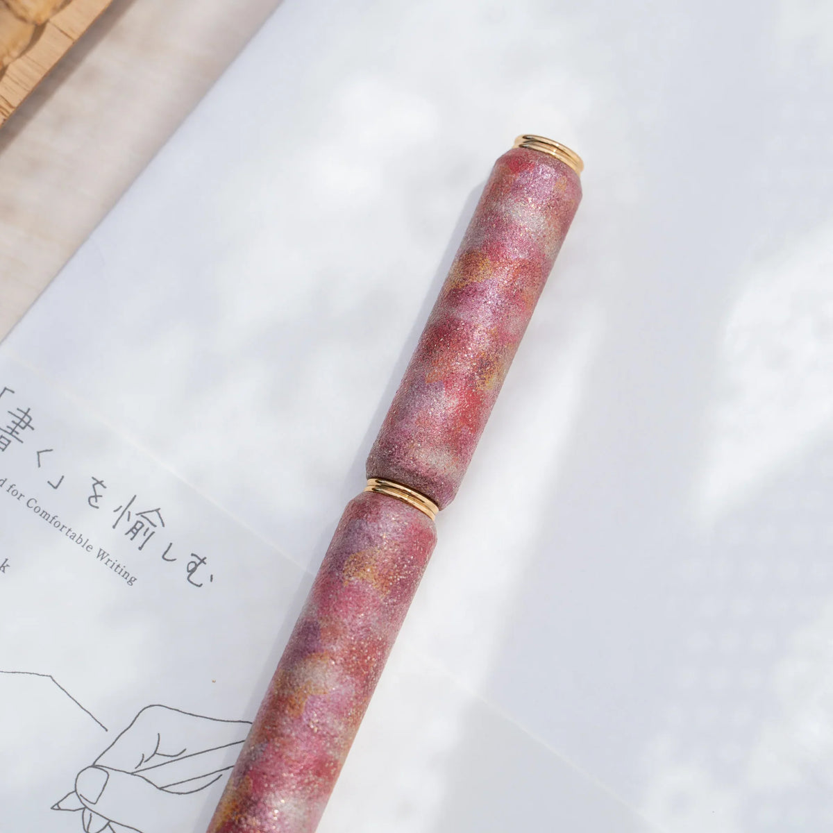 Red marbled urushi lacquered rollerball pen in zelkova wood, resting on a Japanese notebook