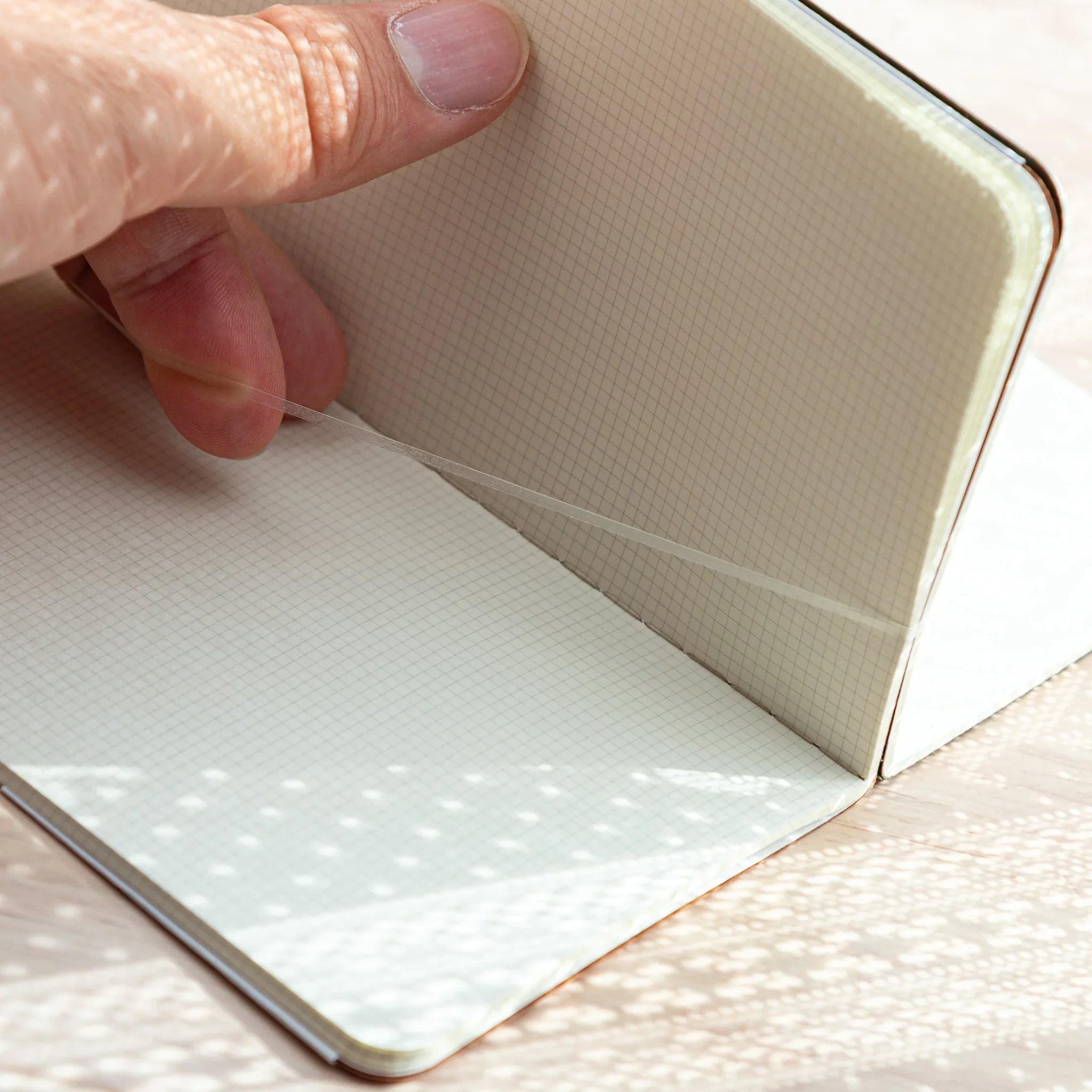 Close-up of RO-BIKI Japanese Note Book with squared grid pages, hand lifting a sheet inside Cool Gray canvas cover.