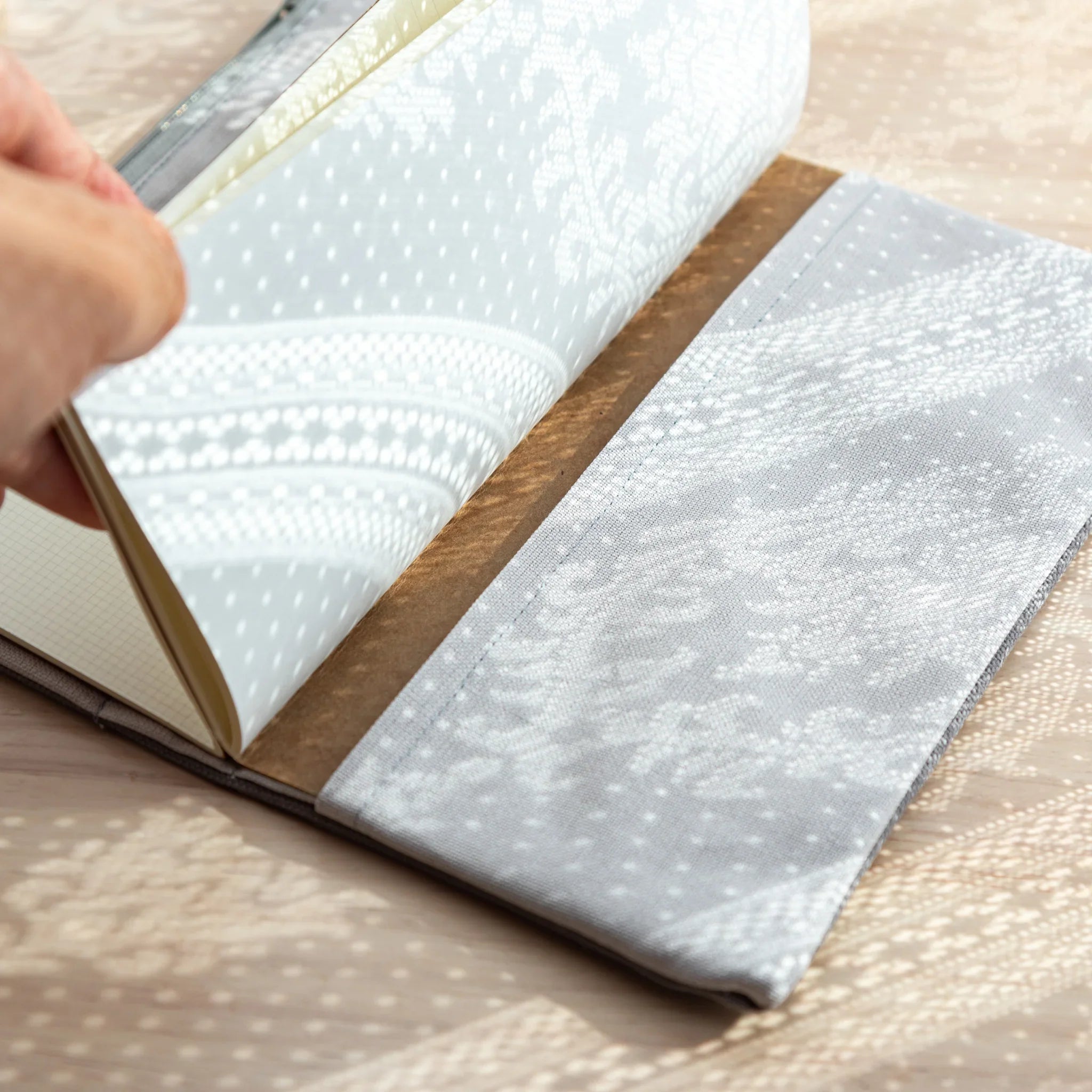 Hand placing RO-BIKI Japanese Note Book into Cool Gray canvas cover, showing notebook fitting securely inside.