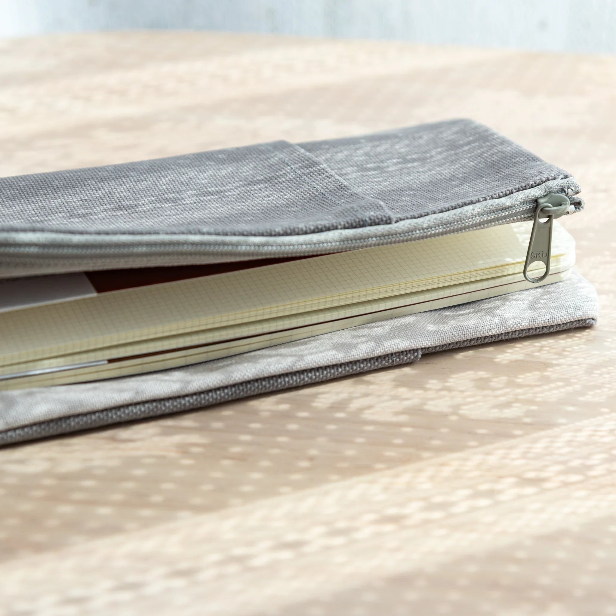 Side view of Cool Gray canvas cover zipped halfway, revealing squared RO-BIKI Japanese Note Book inside.