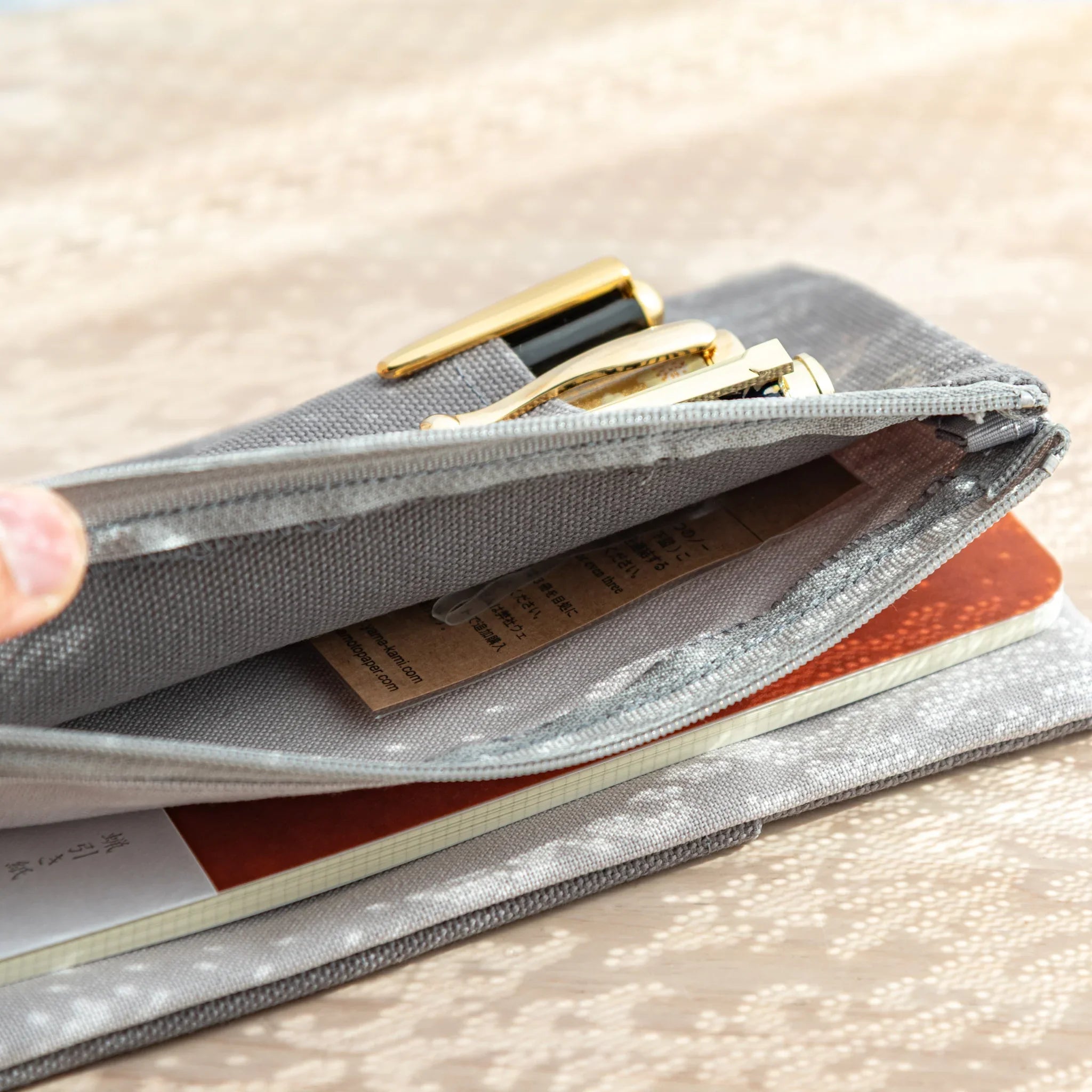 Zippered pocket of RO-BIKI Canvas Cover Cool Gray partially open, showing Japanese Note Book and stationery inside.