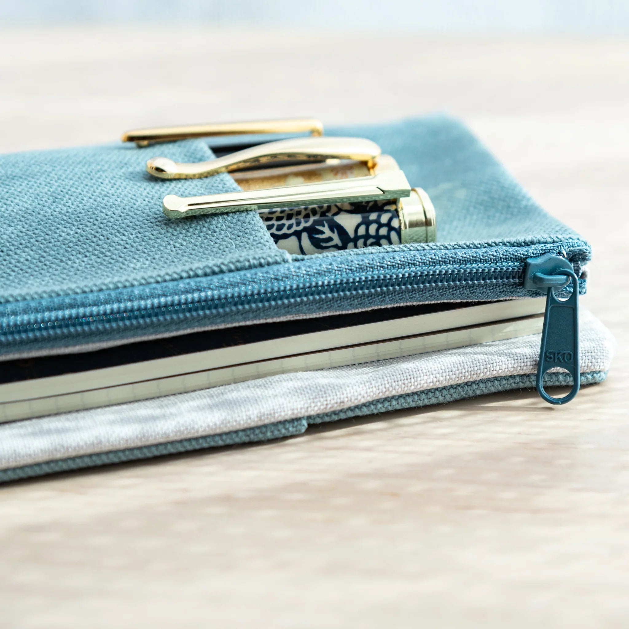 Close-up of blue canvas Japanese Note Book Cover with zipper, holding pens and a notebook securely inside.