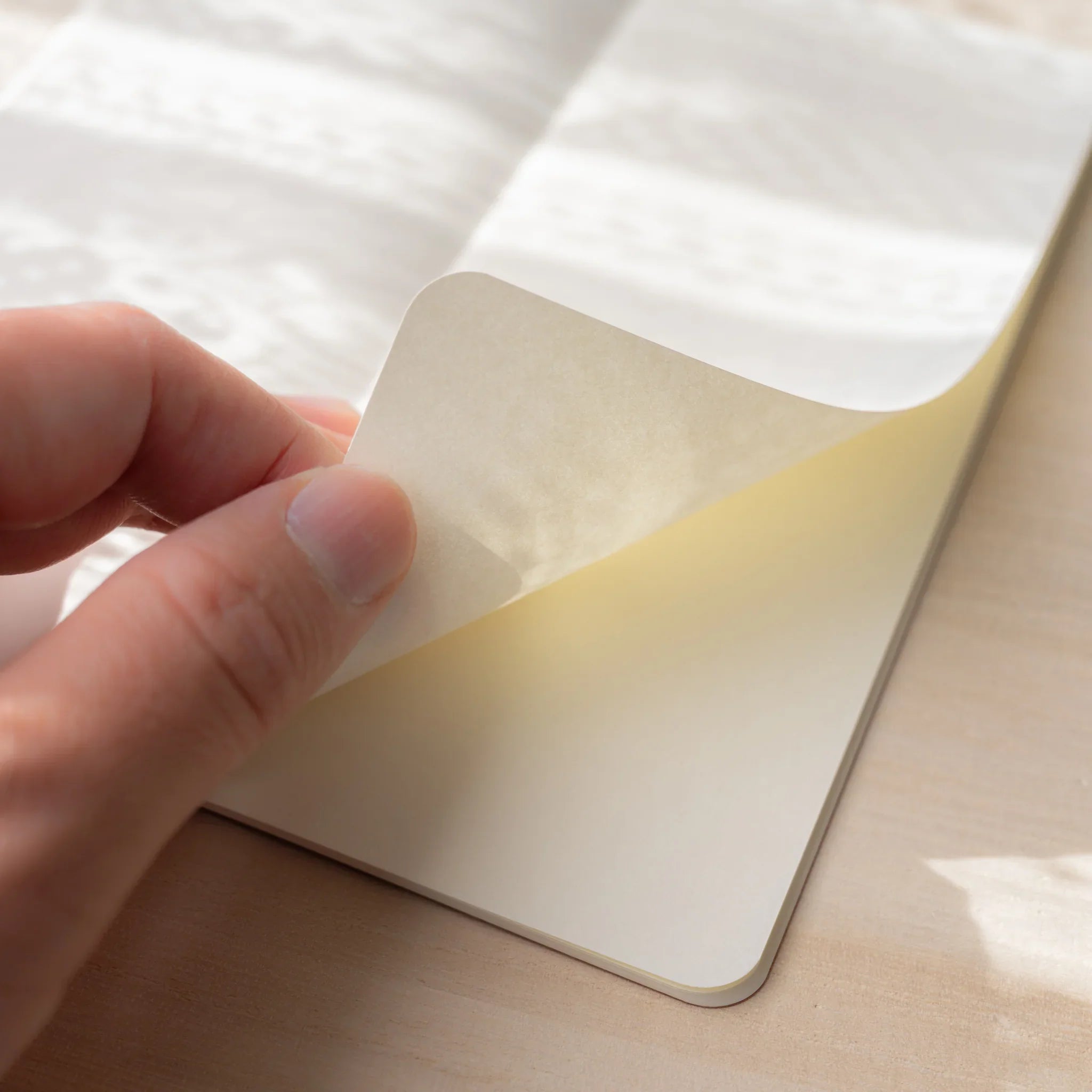 Hand lifting a page of RO-BIKI NOTE Edocha Brown notebook showing thin smooth Soliste paper quality and texture