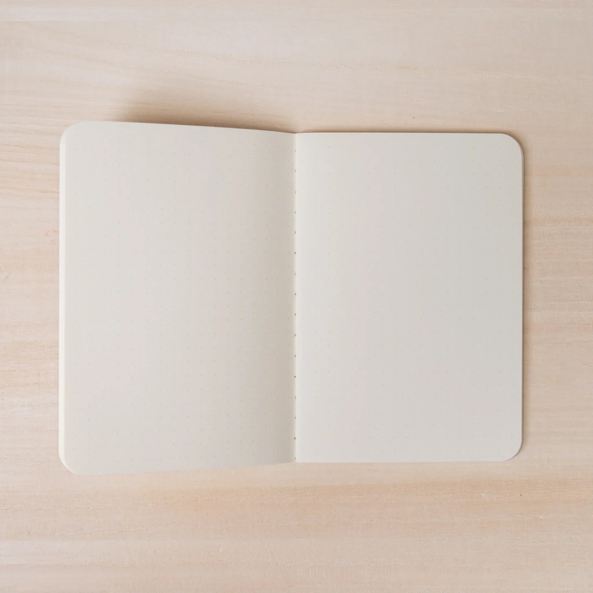 Hand peeling back corner of ivory dot grid page in RO-BIKI NOTE, showing paper thickness and rounded corners