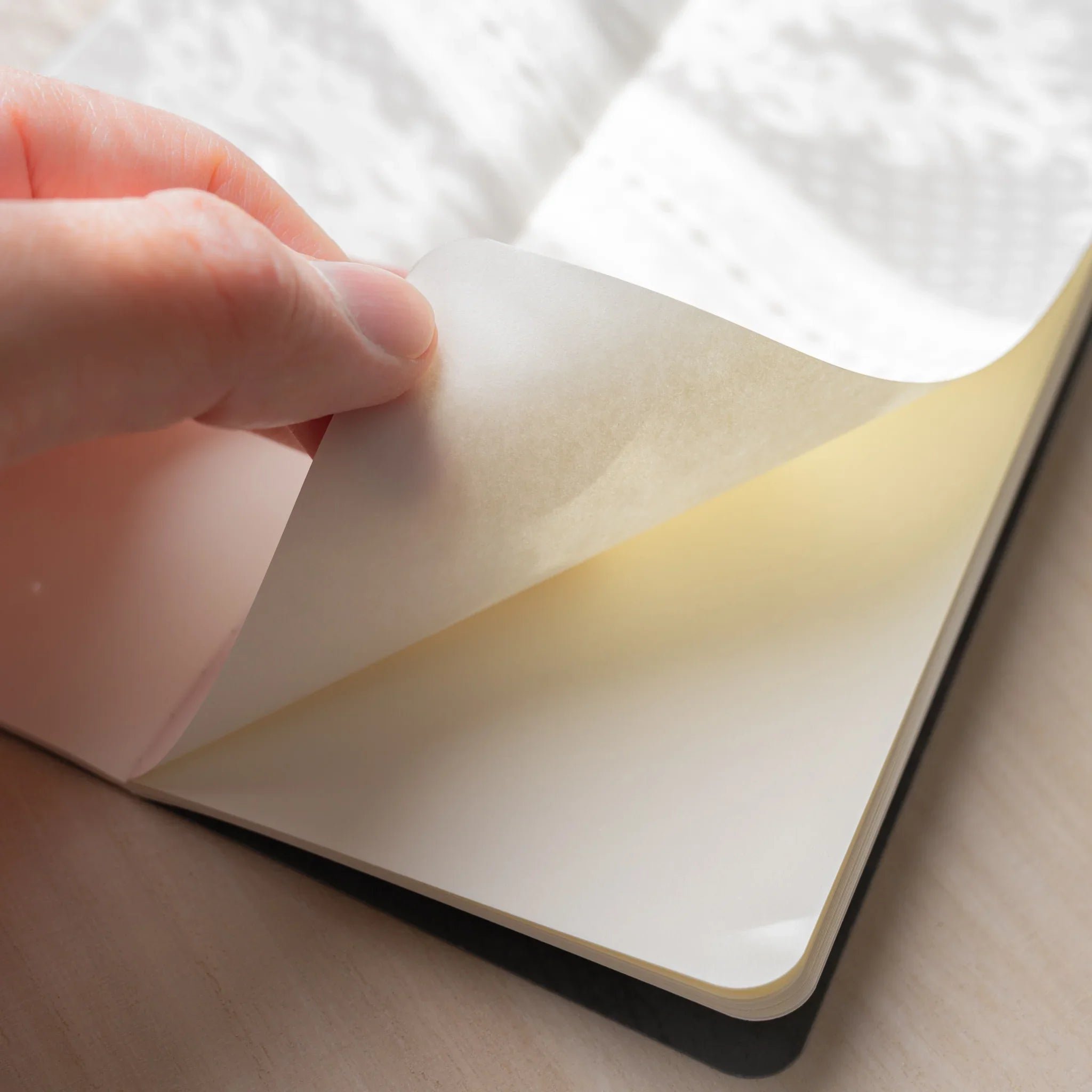 Hand lifting translucent glassine interleaf page from RO-BIKI NOTE Ginnezu gray wax-coated blank notebook