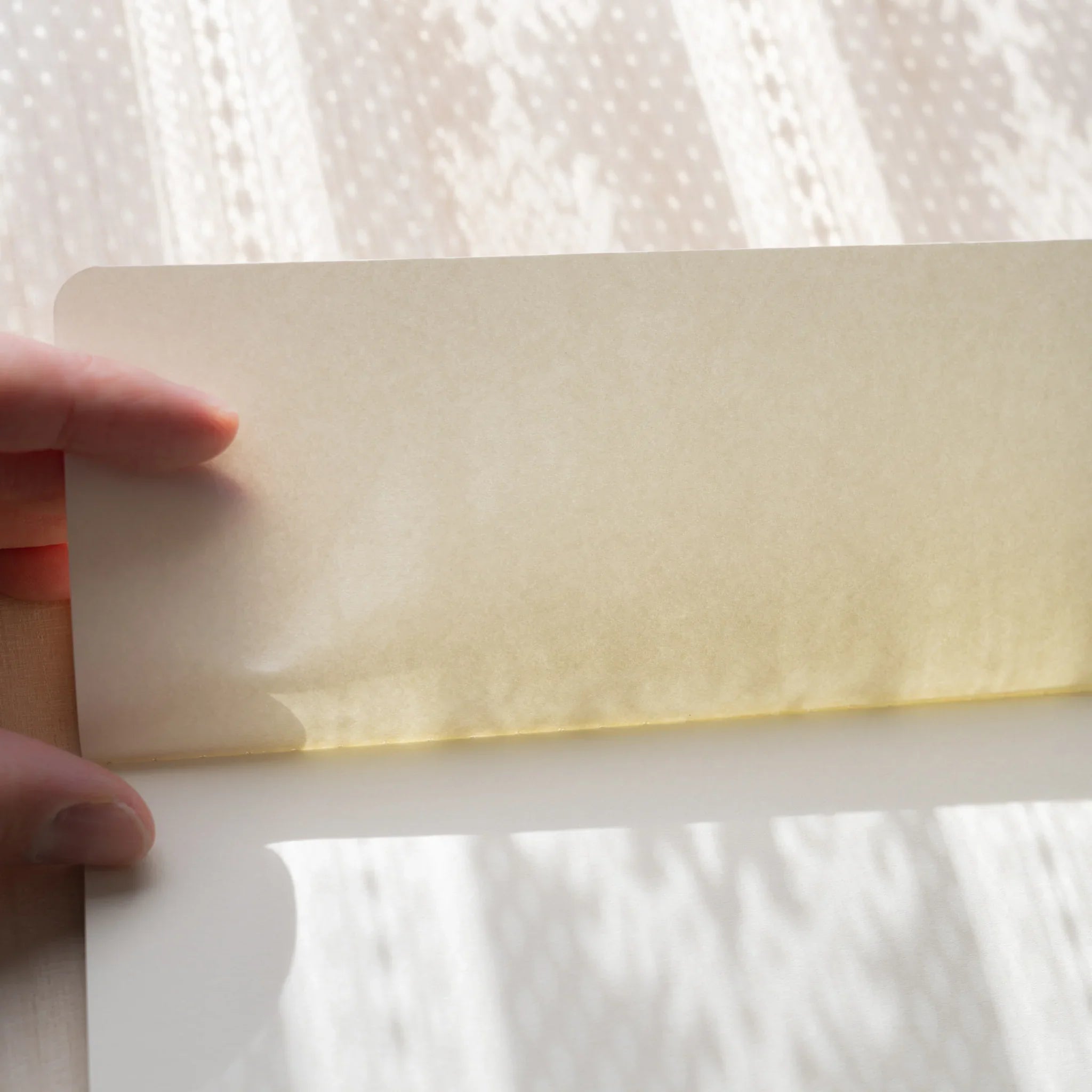 Hand holding up semi-transparent glassine paper sheet from RO-BIKI NOTE Ginnezu gray Japanese wax-coated notebook