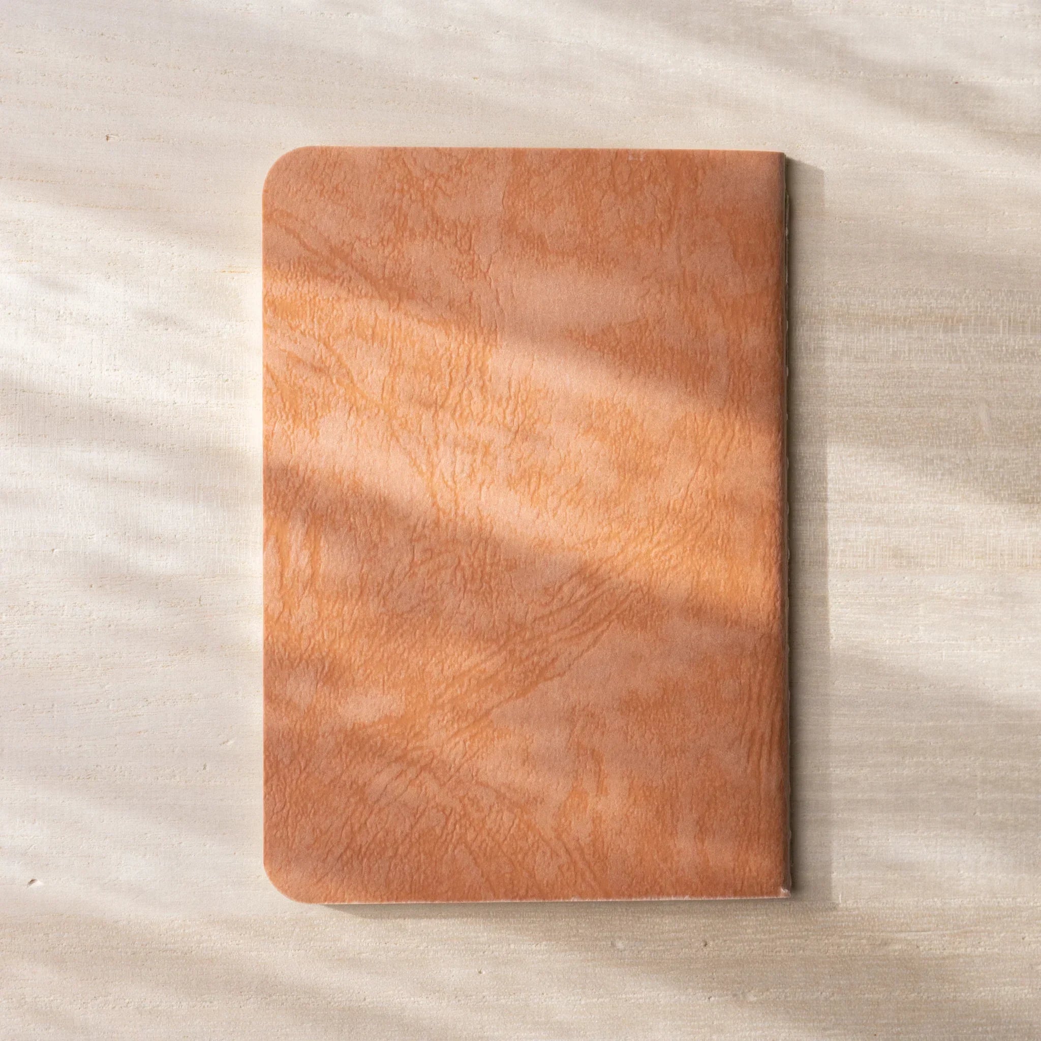 RO-BIKI NOTE stacked closed, showing hanezu red waxed cover, rounded corners, textured Japanese craft feel