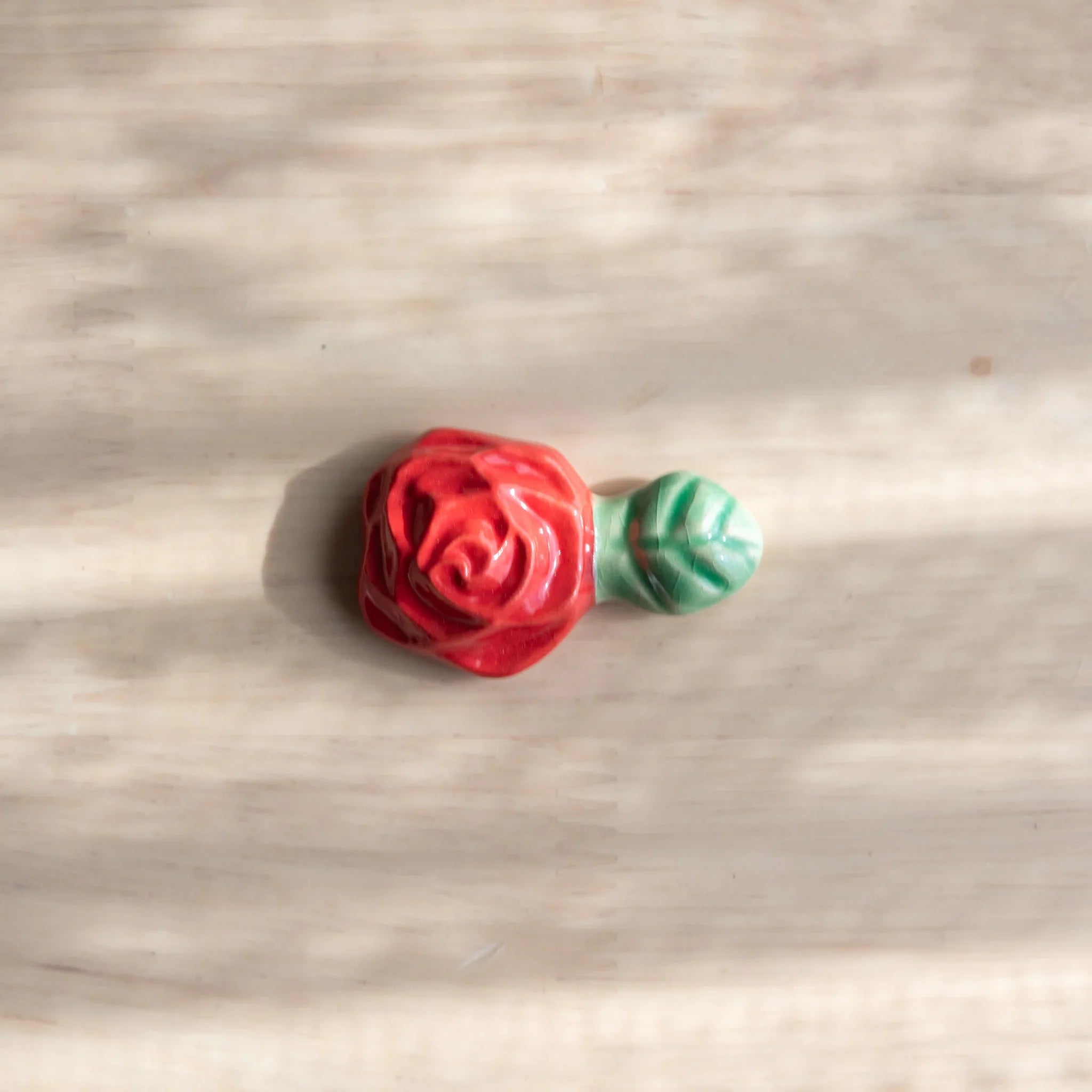 Collection of red and pink rose-shaped handcrafted ceramic pen rests in varying color tones on wooden surface detail