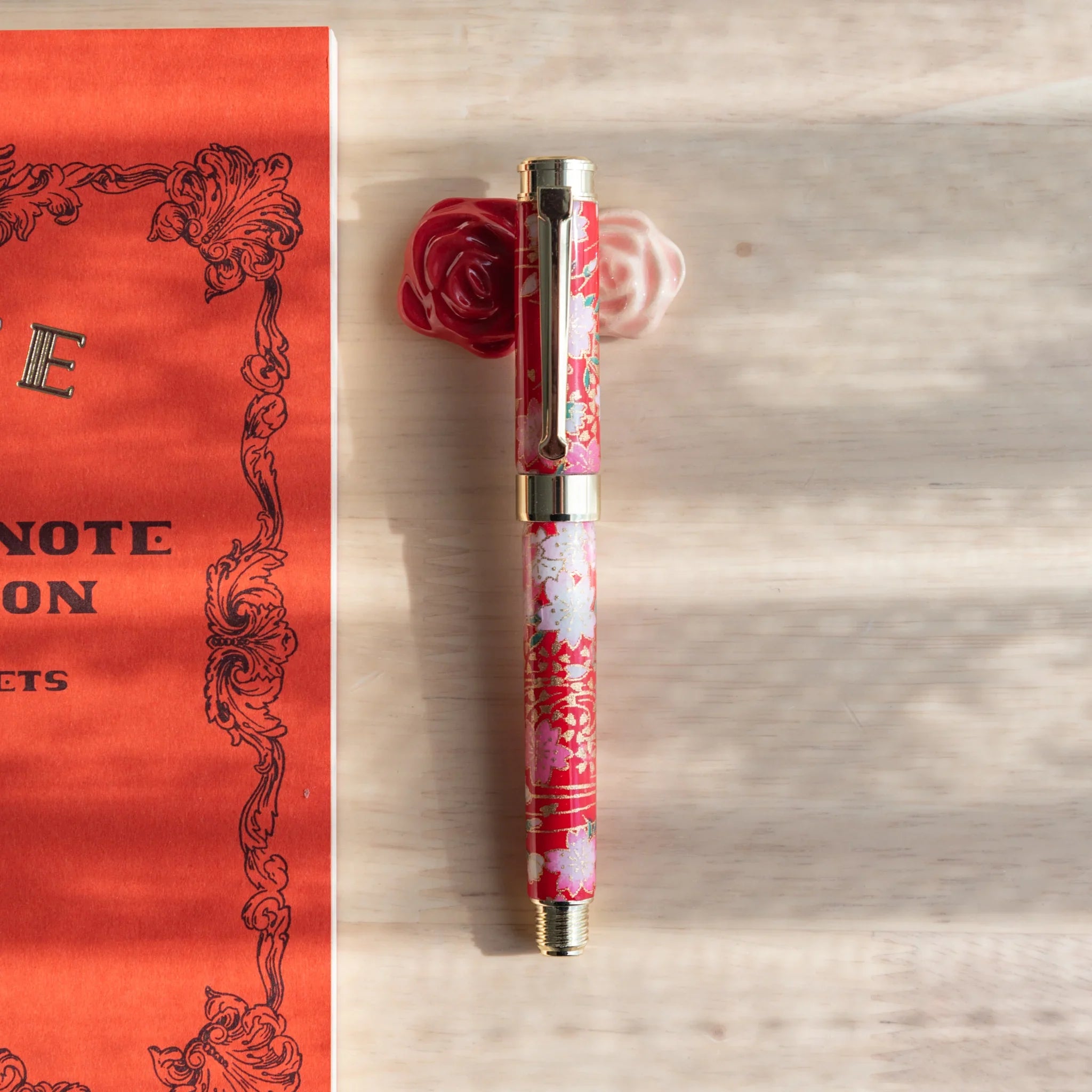 Pink rose-shaped handcrafted ceramic pen rest with green leaf accent, delicate miniature Japanese design close shot