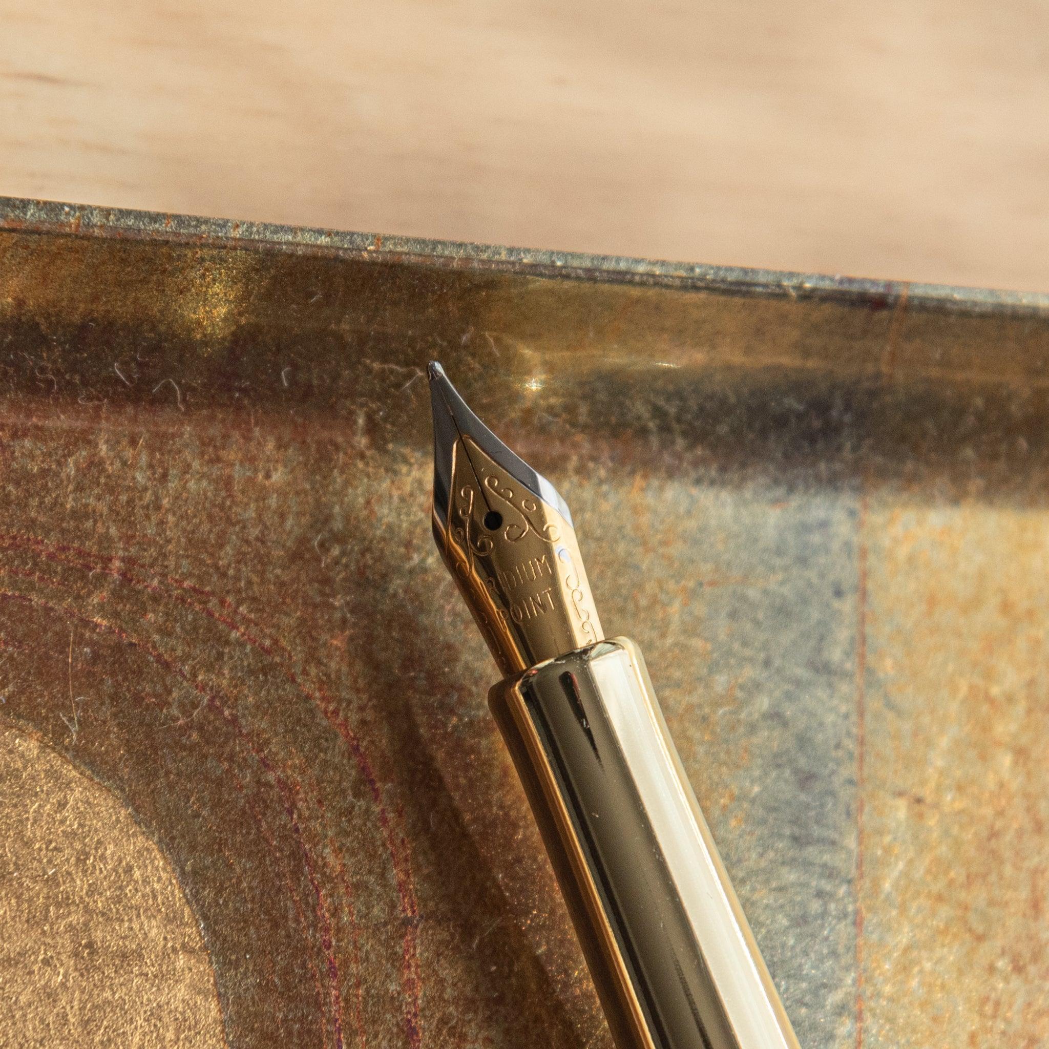 Gold nib of Japanese fountain pen with intricate detailing, positioned on a reflective golden tray under sunlight.