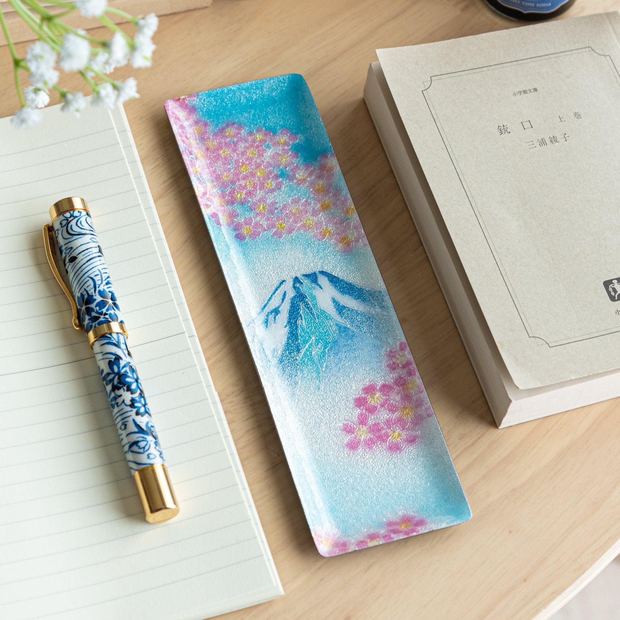 Narrow rectangular tray with Mount Fuji and pink cherry blossom design, displayed with books, a notebook, and a blue-patterned pen.