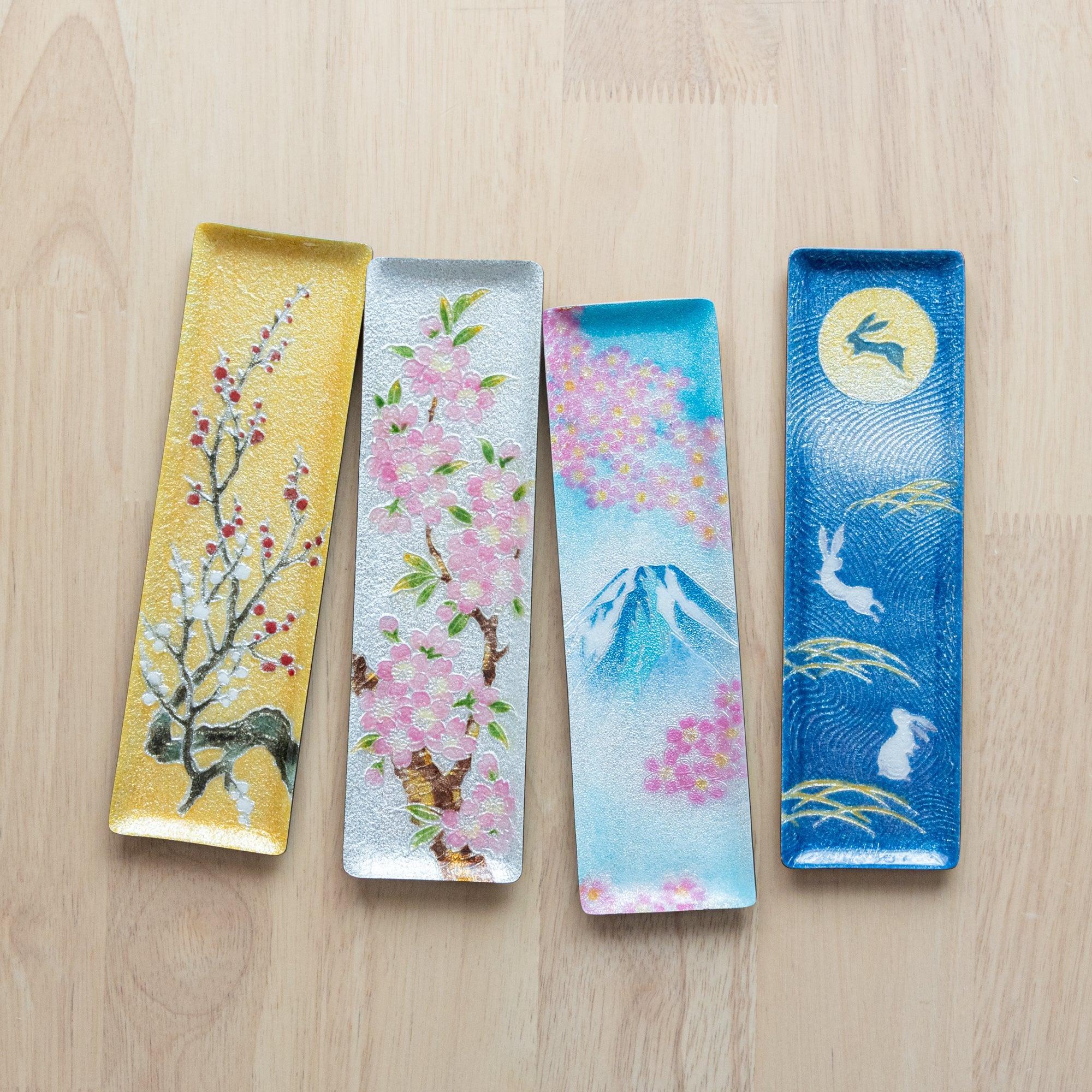 Four Japanese shippo ware slim pen trays: plum on gold, sakura on silver, Mt. Fuji with sakura, and rabbit under moon on blue