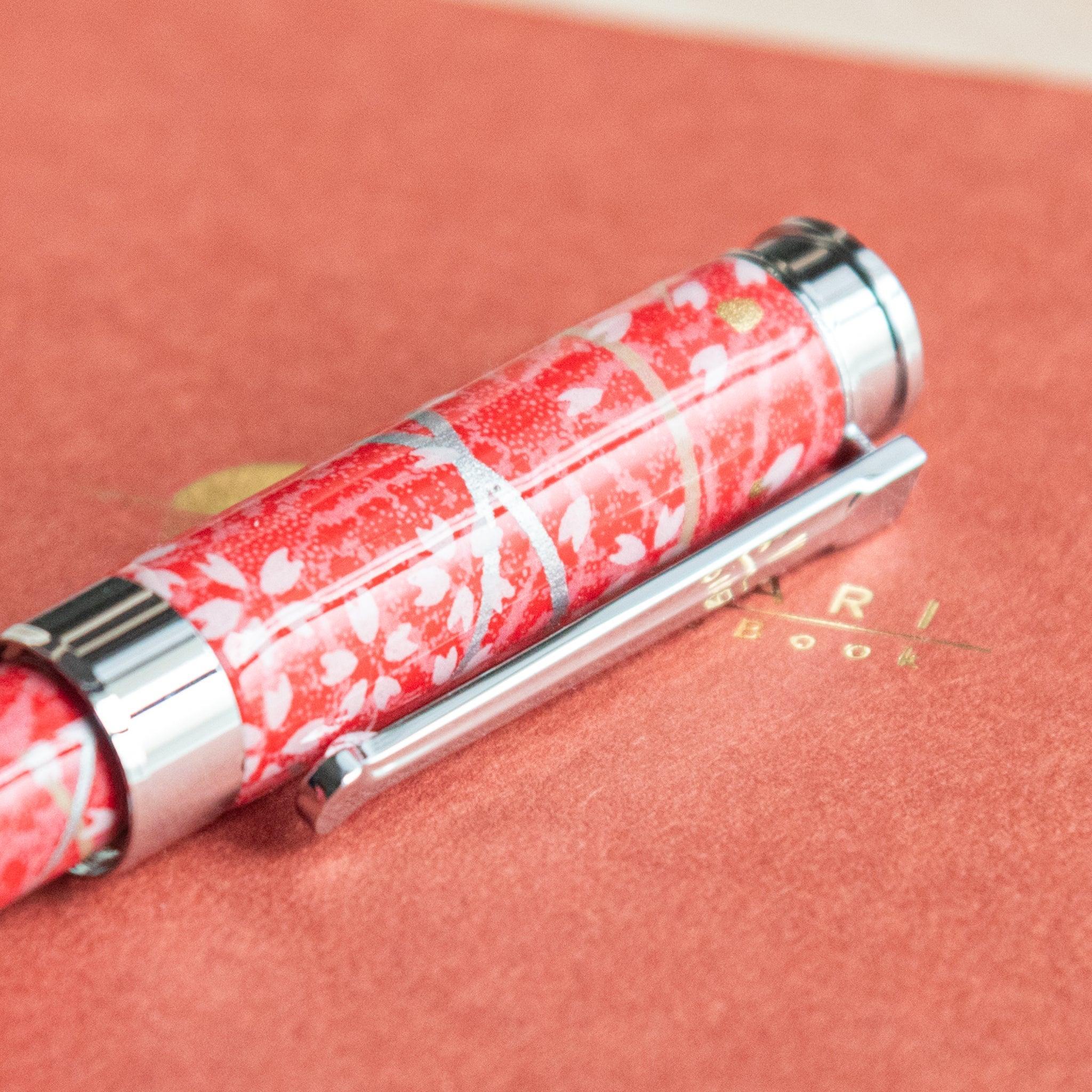 Detailed view of the red-patterned cap of a Japanese stationery fountain pen with silver accents, placed on an orange notebook.