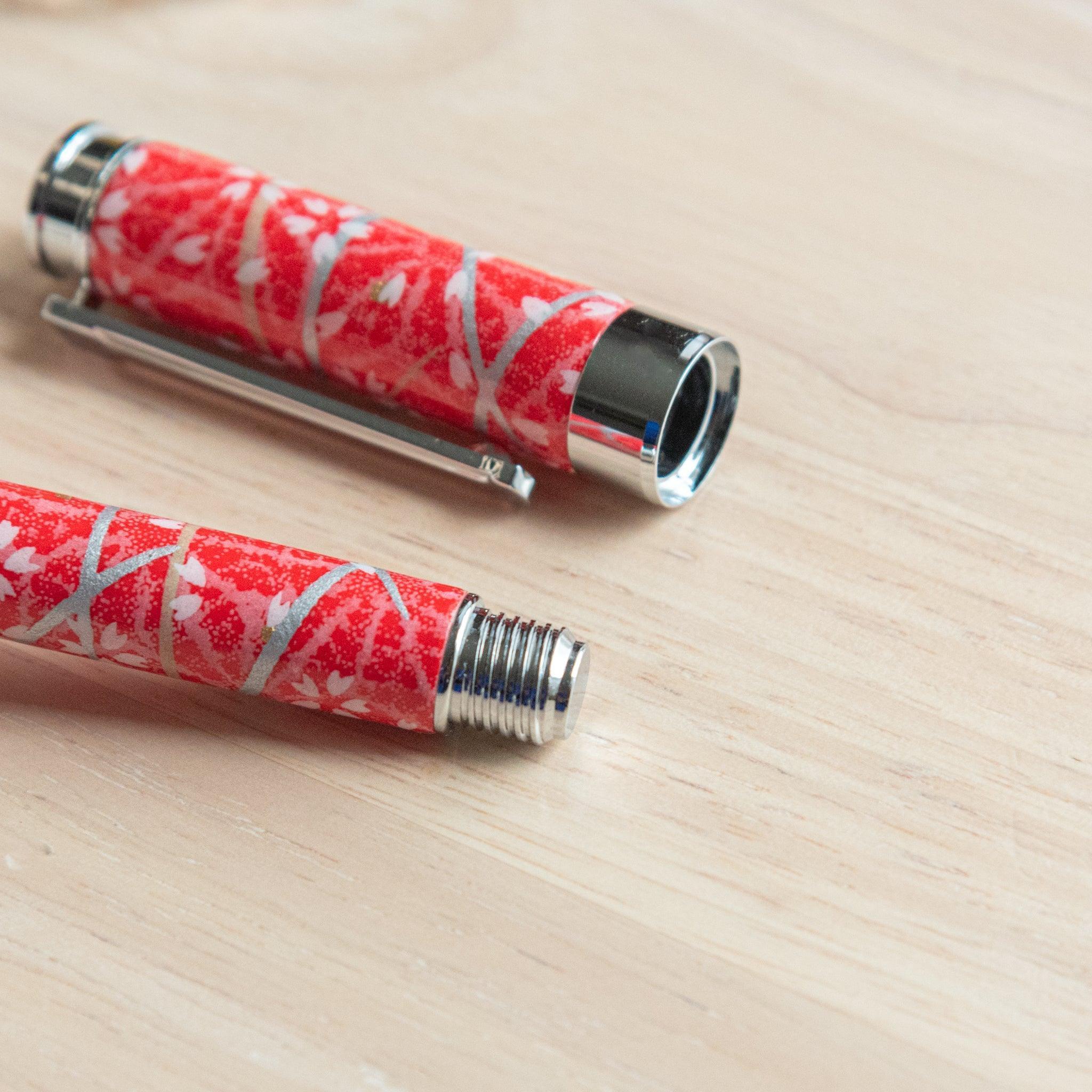 A Japanese stationery fountain pen with red patterns and silver accents, disassembled, placed on a wooden surface.