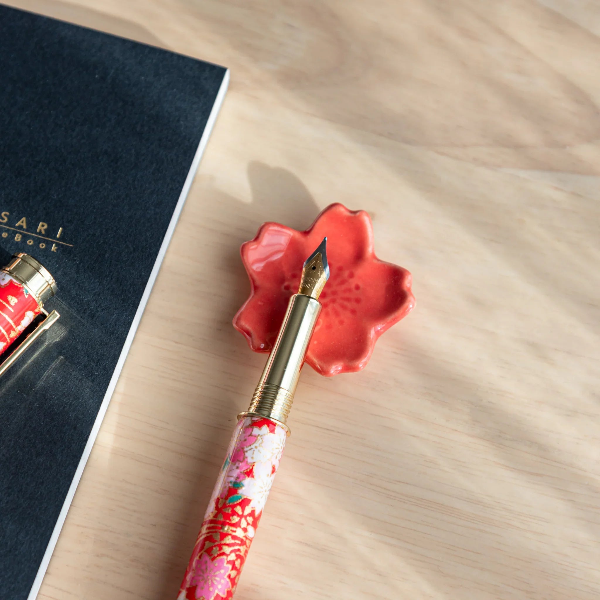 Pale pink sakura handcrafted pen rest featuring traditional five-petal Japanese flower design and form on neutral surface
