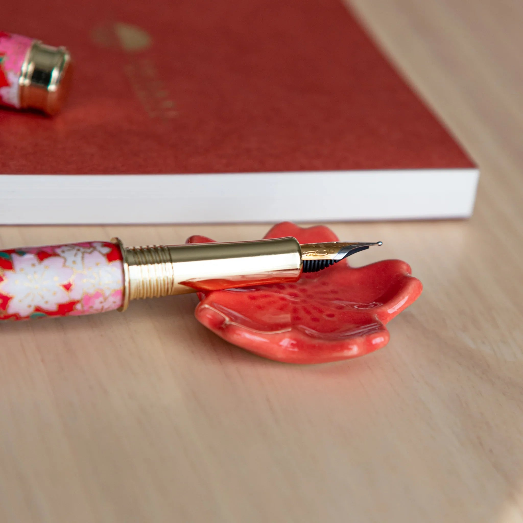 Pink handcrafted sakura flower pen rest with detailed individual petal definition and grooved holder on neutral surface