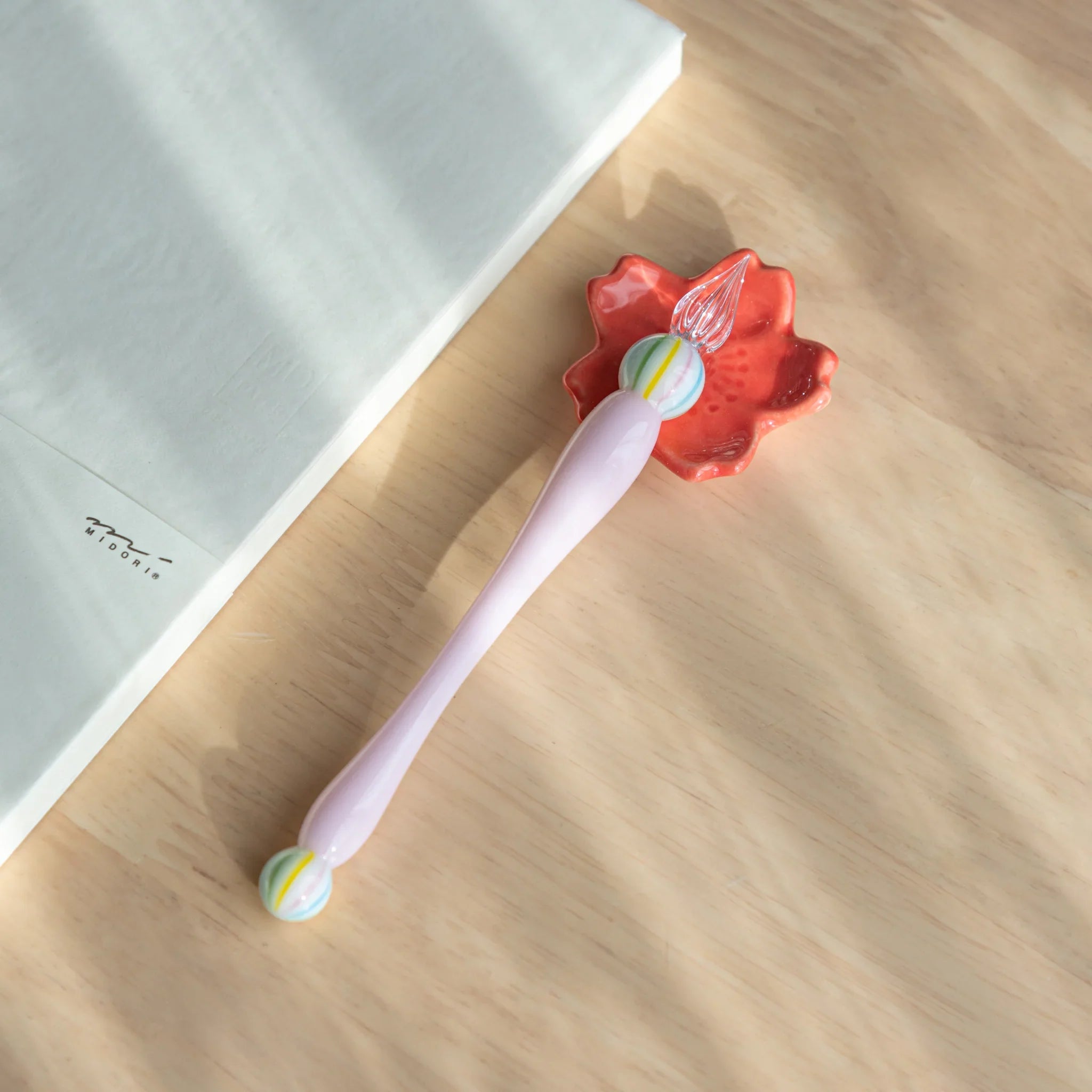 Pale pink handcrafted sakura flower pen rest with clearly defined petals and recessed functional groove on neutral surface
