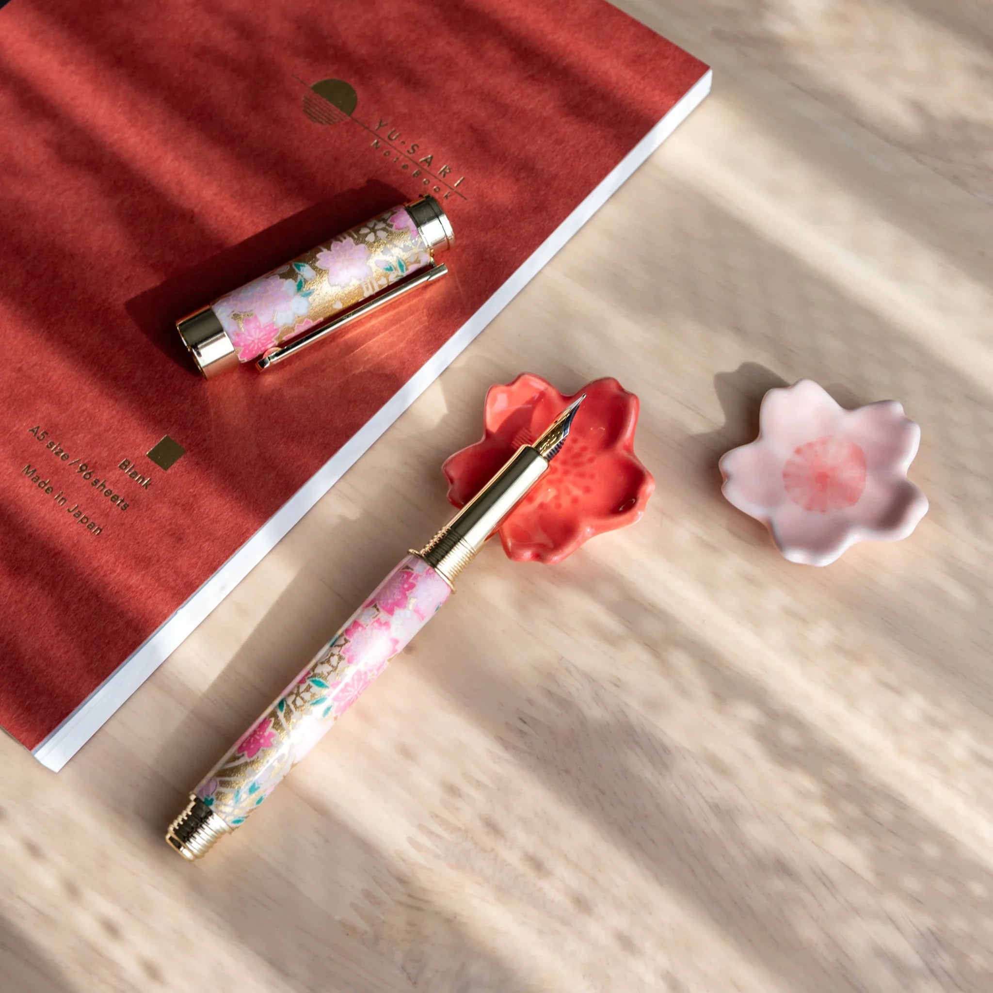 Pink sakura-shaped handcrafted pen rest showing five sculptured petals and functional grooved interior on neutral surface